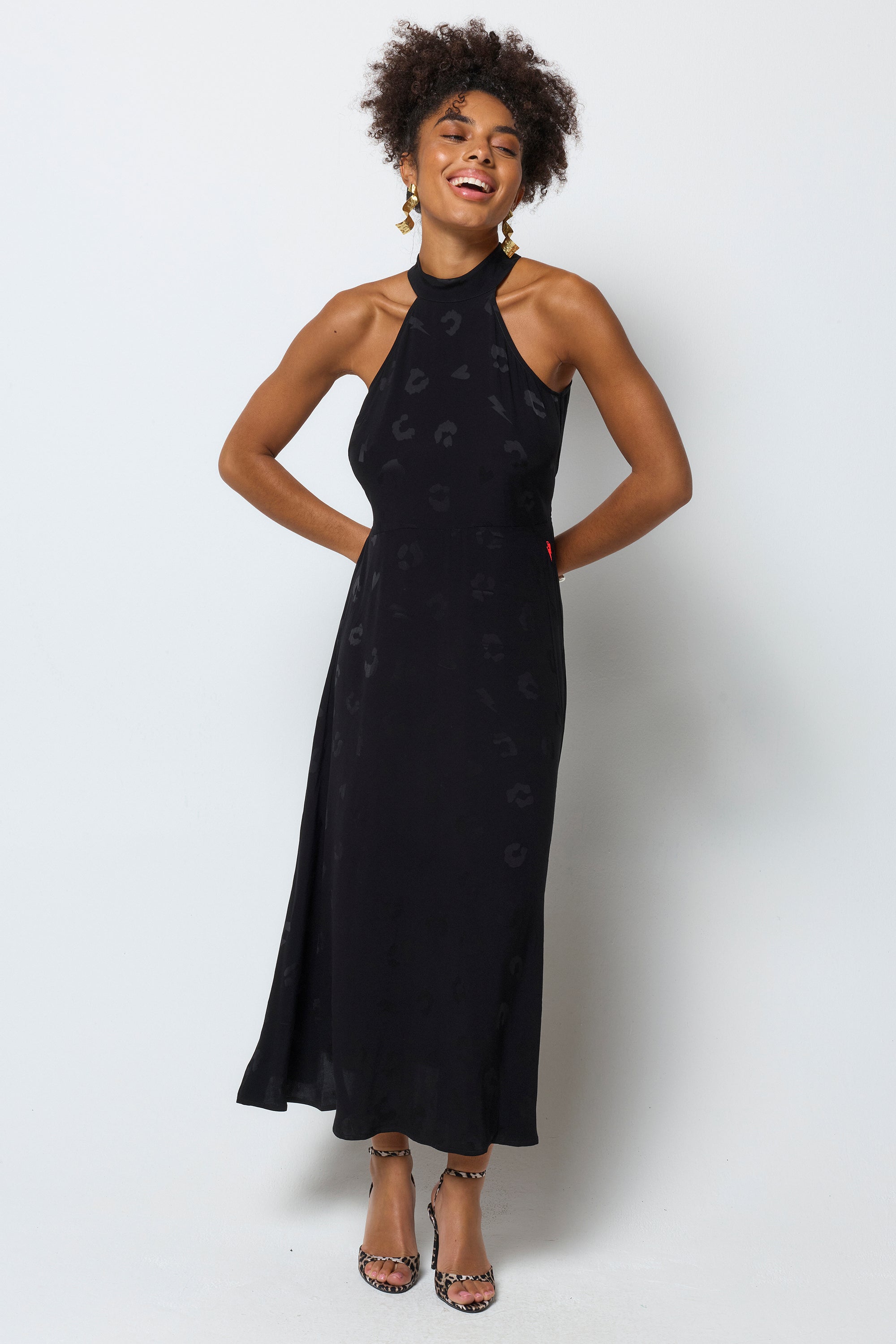 Scamp & Dude Black Jacquard Halter Midi Dress | Model wears a black halterneck dress in a leopard jacquard print. Worn with printed heels and gold jewellery.