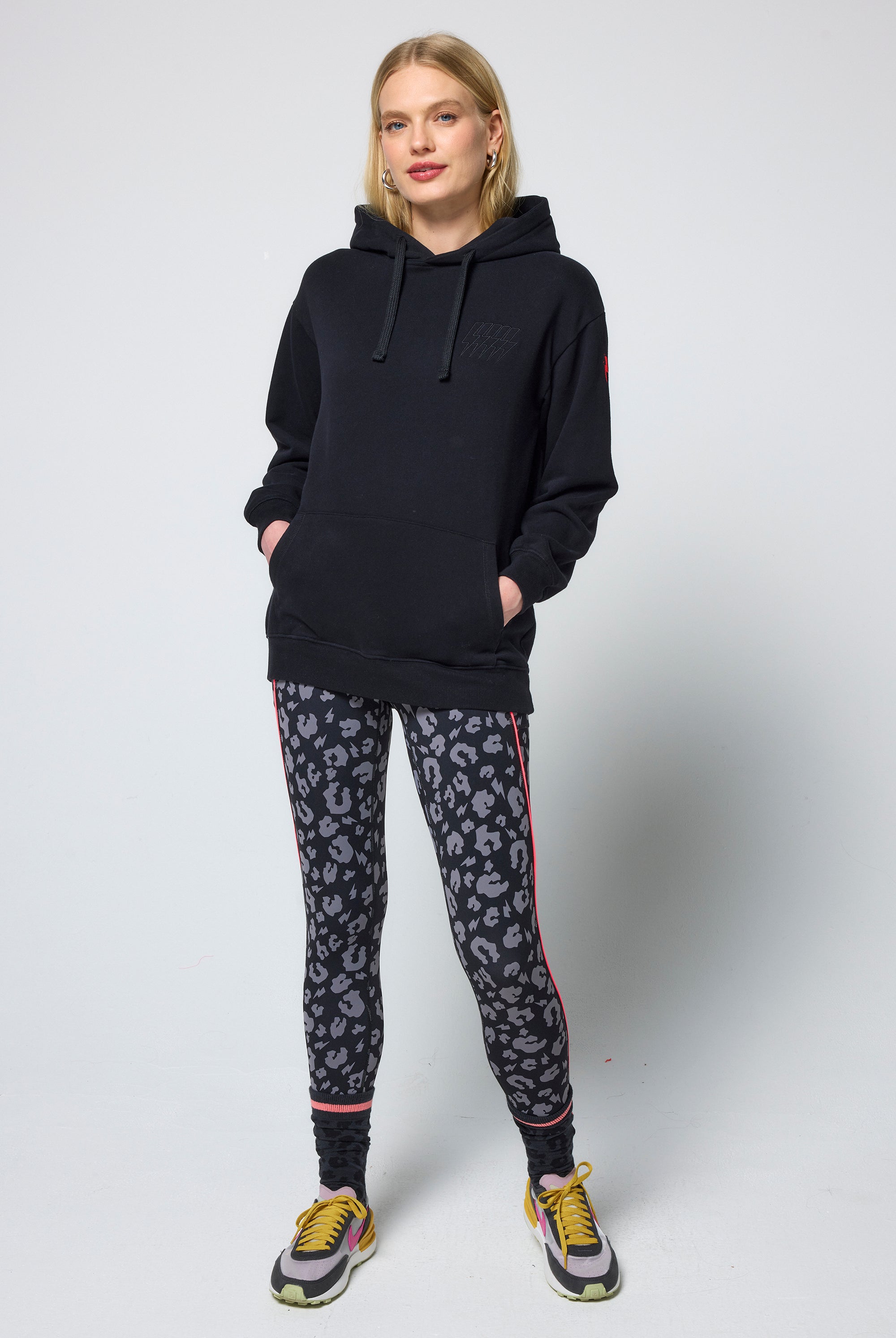 Scamp & Dude Black Multi Neon Bolt Longline Hoodie | Model wearing a black hoodie and patterned leggings on a white background.