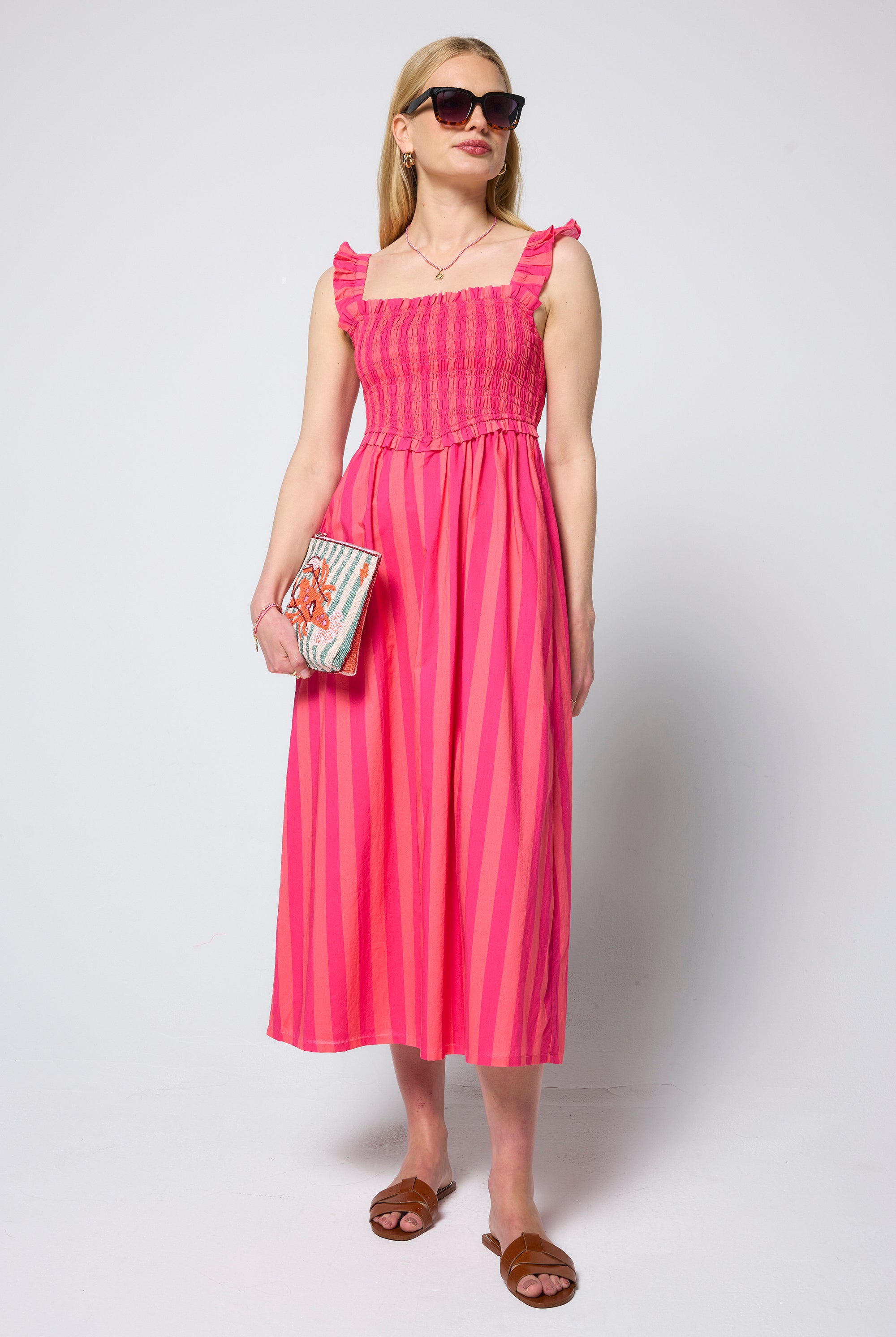 Scamp & Dude Pink and Coral Stripe Corset Sundress | Model wearing a pink and coral stripe corset dress holding a beaded stripe bag.