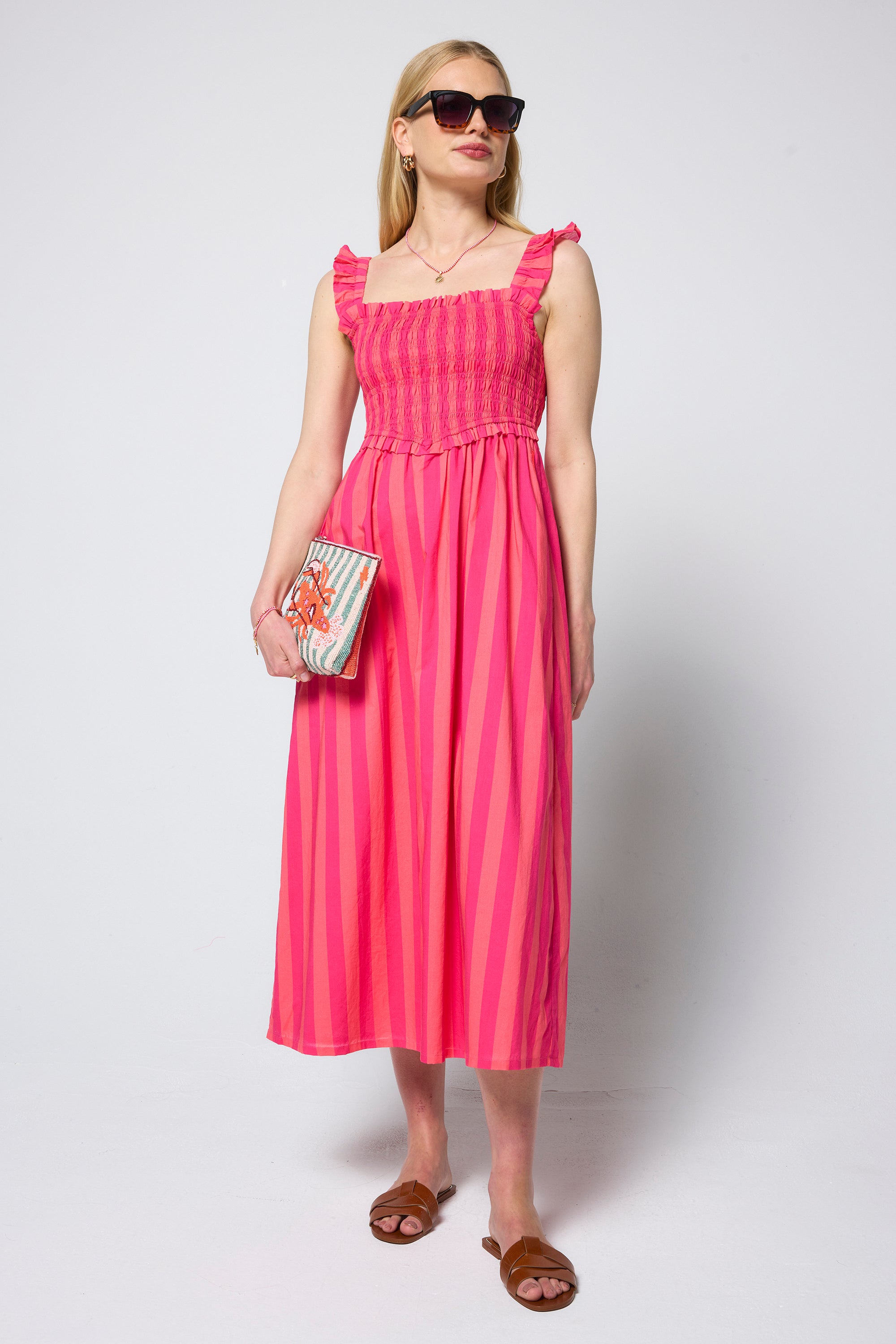 Scamp & Dude Pink and Coral Stripe Corset Sundress | Model wearing a pink and coral stripe corset dress holding a beaded stripe bag.