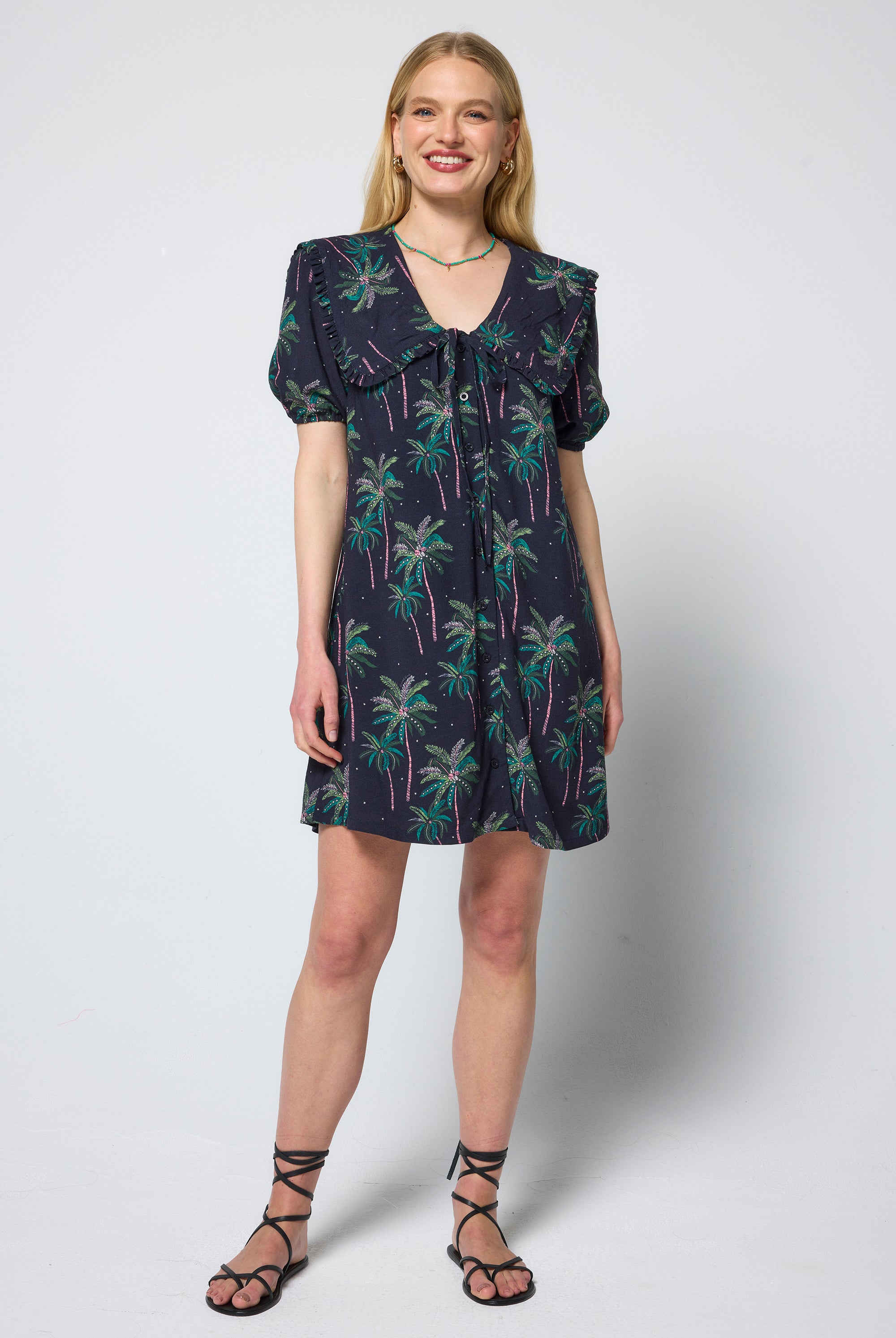 Scamp & Dude Navy Midnight Palm Collared Short Dress | Model wearing a short dress in a navy palm print with peter pan collar and tie front detail. Worn with black sandals.