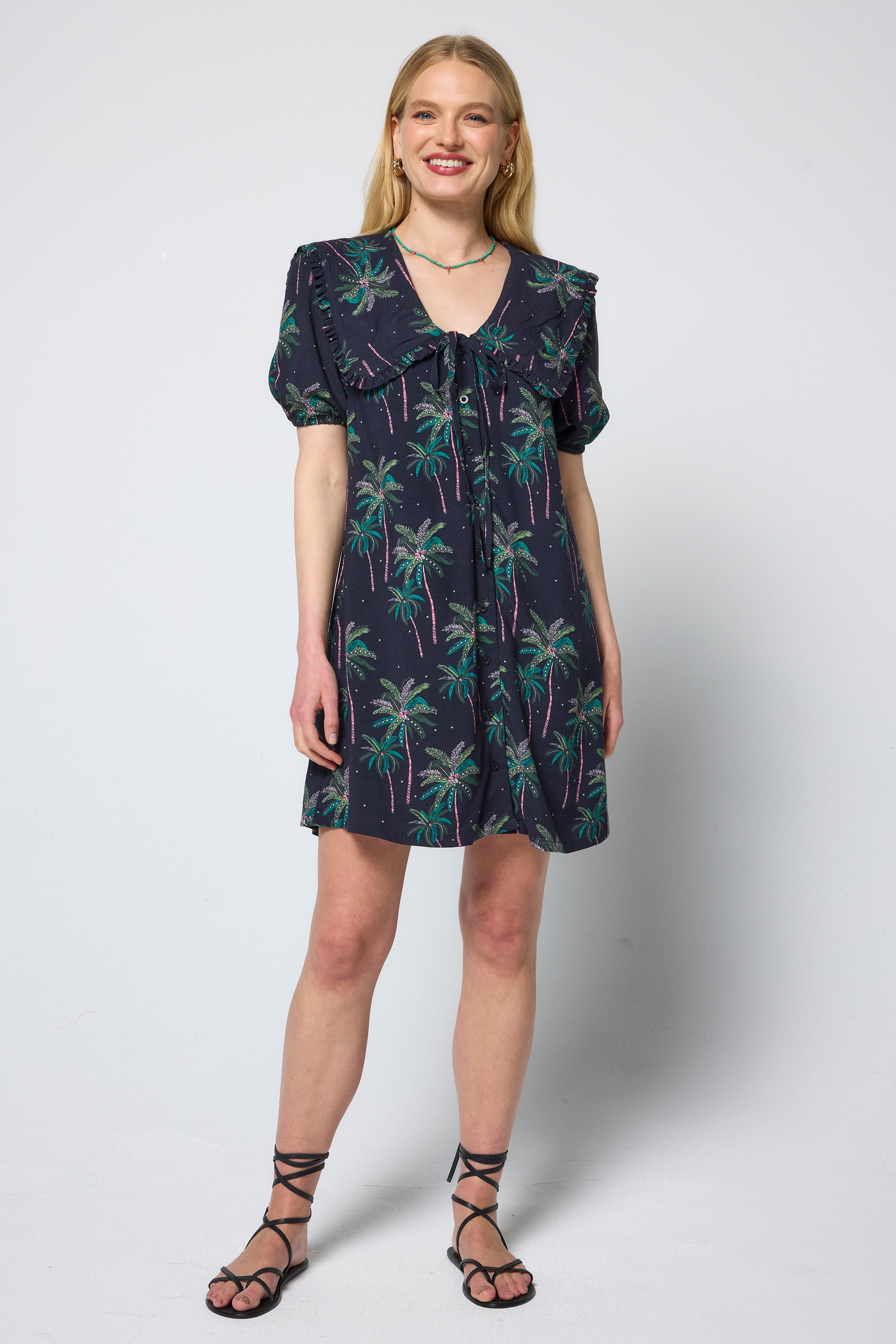 Scamp & Dude Navy Midnight Palm Collared Short Dress | Model wearing a short dress in a navy palm print with peter pan collar and tie front detail. Worn with black sandals.