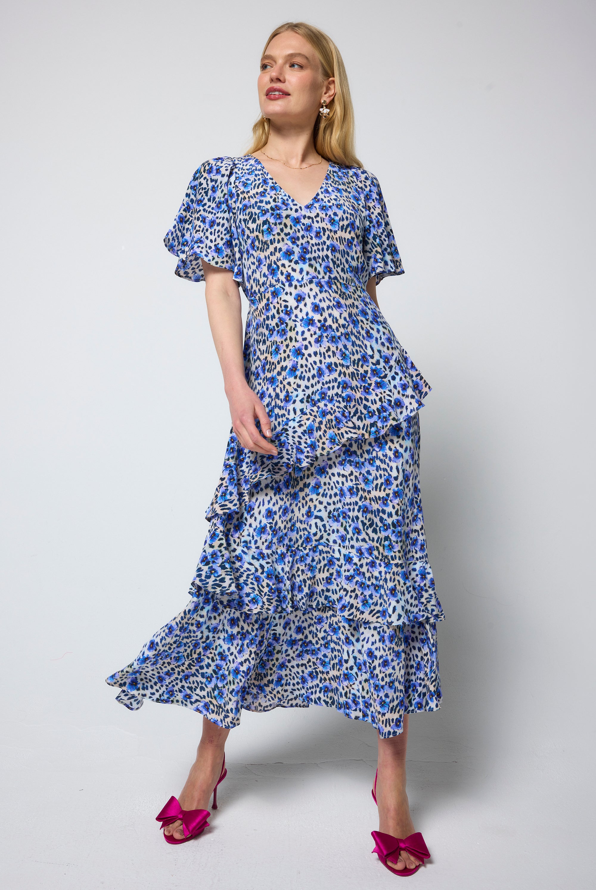 Scamp and Dude White with Blue Paradise Cheetah Ruffle Detail Maxi Dress | Model wearing a white v-neck maxi dress with blue and black floral animal print. Worn with pink bow heels.