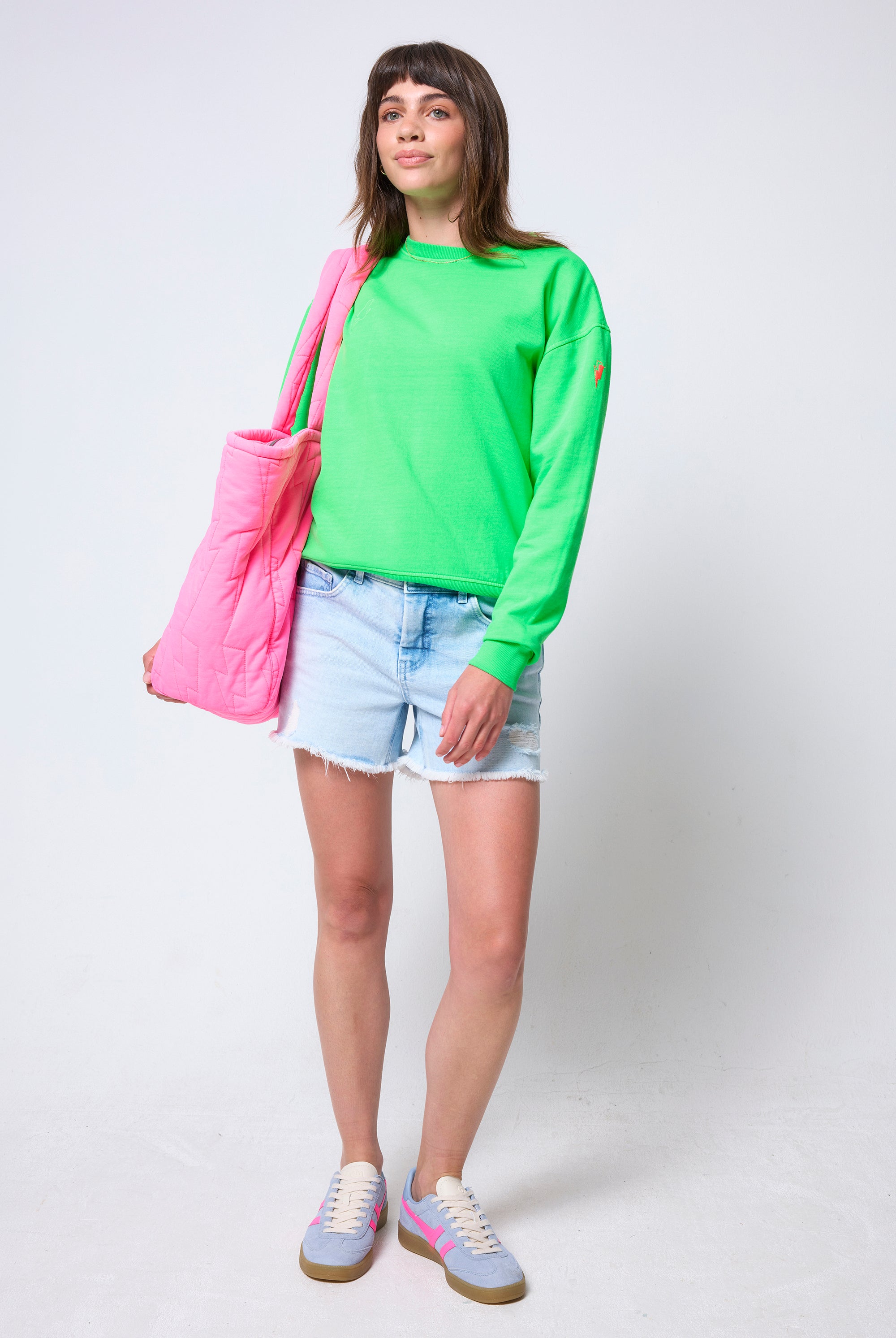 Scamp & Dude Neon Green Washed Ultimate Sweatshirt | Model wearing a bright green sweatshirt, denim shorts, and blue trainers, holding a pink bag.