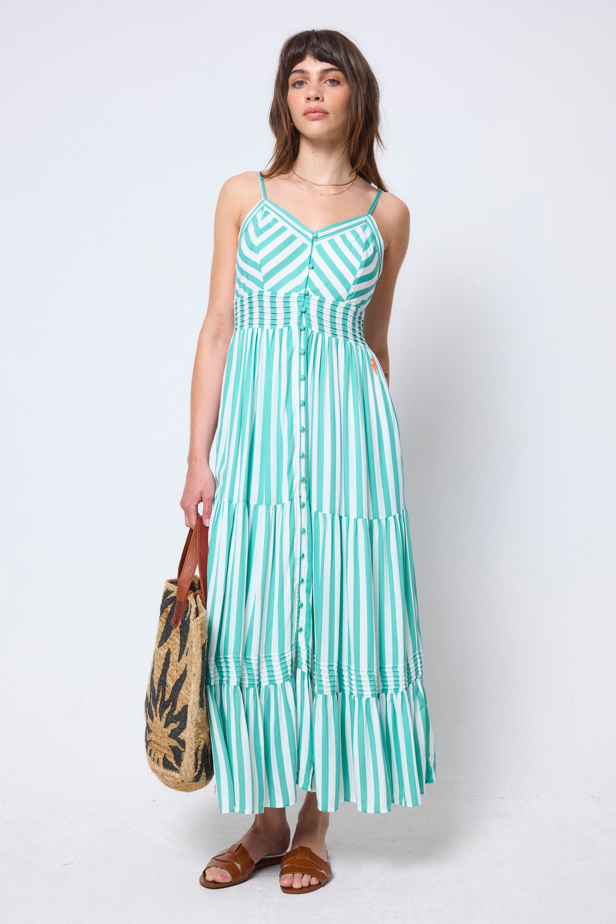 Scamp & Dude Green and White Stripe Pintuck Midi Sundress | Model wearing a green and white striped dress holding a woven bag on a white background.