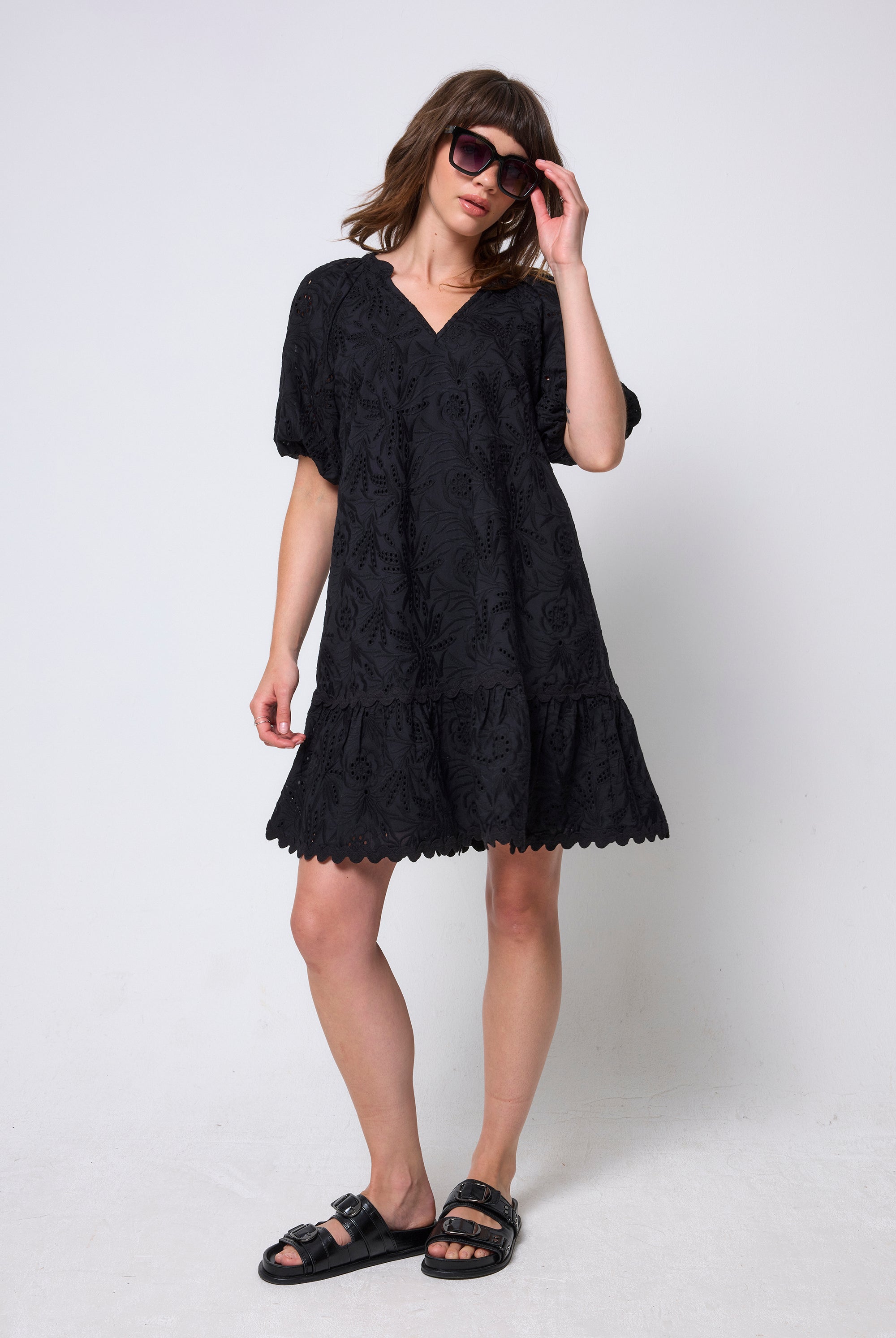 Scamp & Dude Black V-Neck Broderie Short Dress | Model wearing a black broderie mini dress with black sandals.