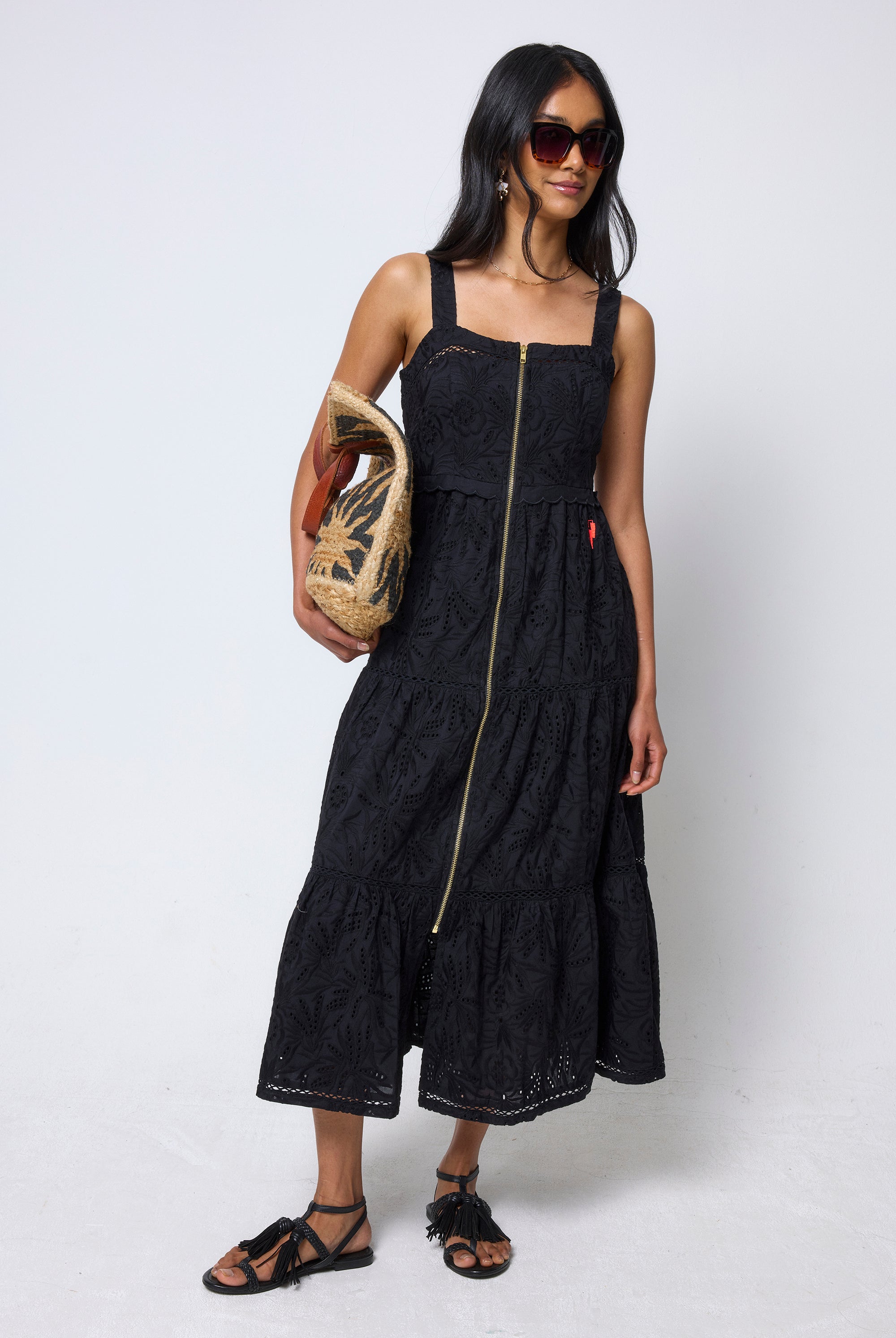 Scamp & Dude Black Broderie Zip Detail Midi Sundress | Model wearing a black dress with a zipper, holding a woven bag on a white background.