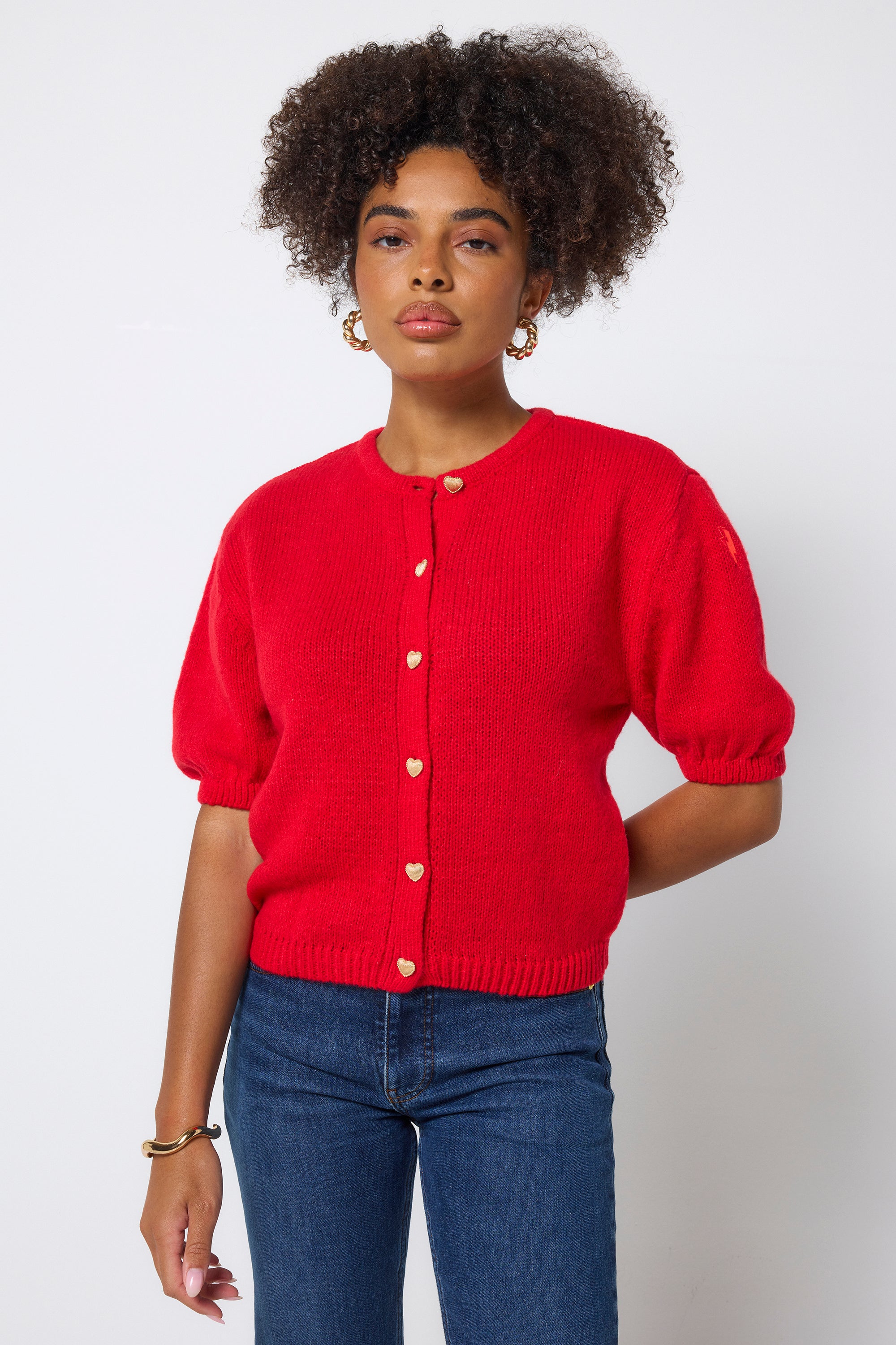 Scamp & Dude Red Short Sleeve Cardigan | Model wearing a red cardigan with gold heart buttons and blue jeans.