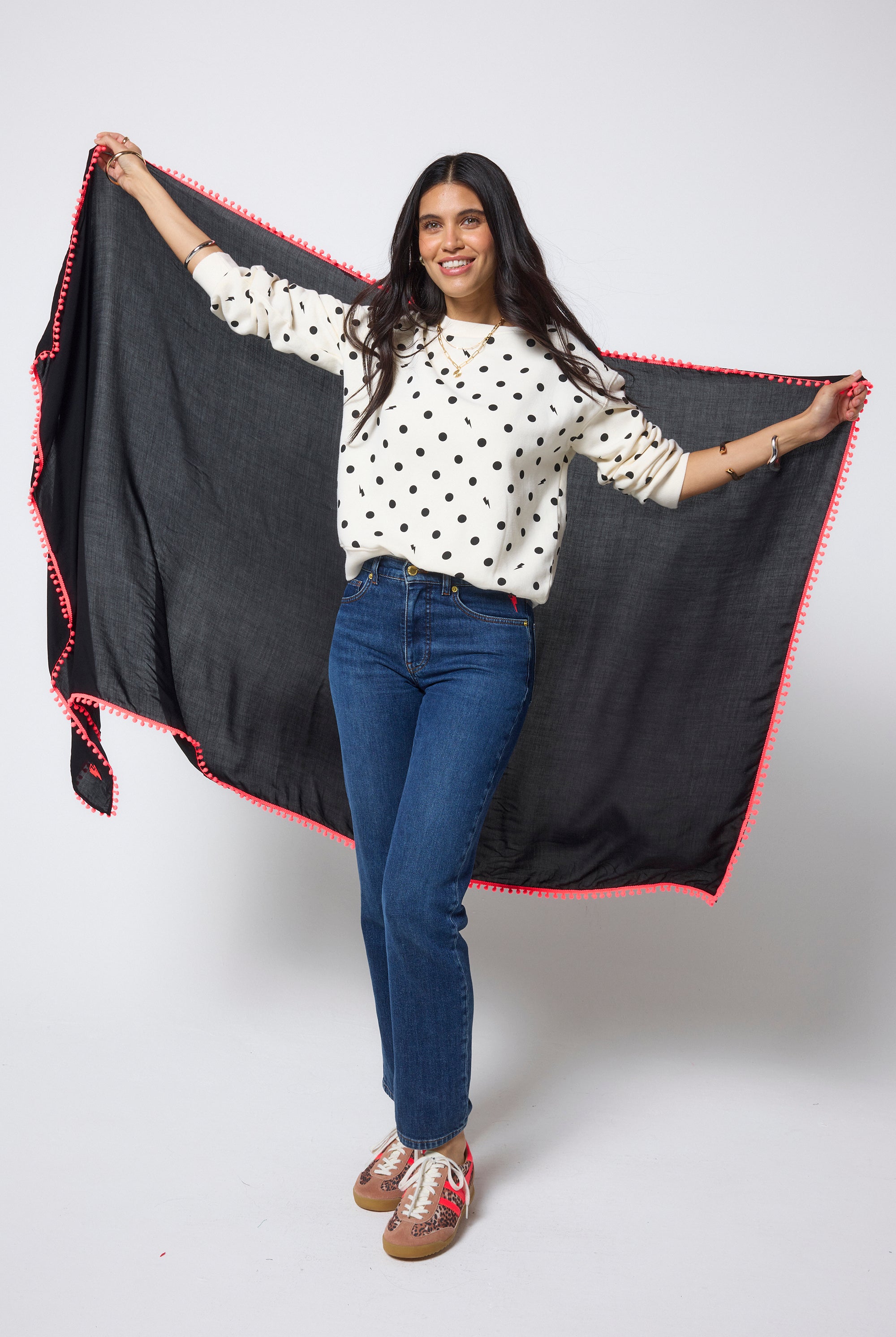 Scamp & Dude Black Charity Super Scarf | Model holding a black scarf with neon coral pom pom trim against a white background.