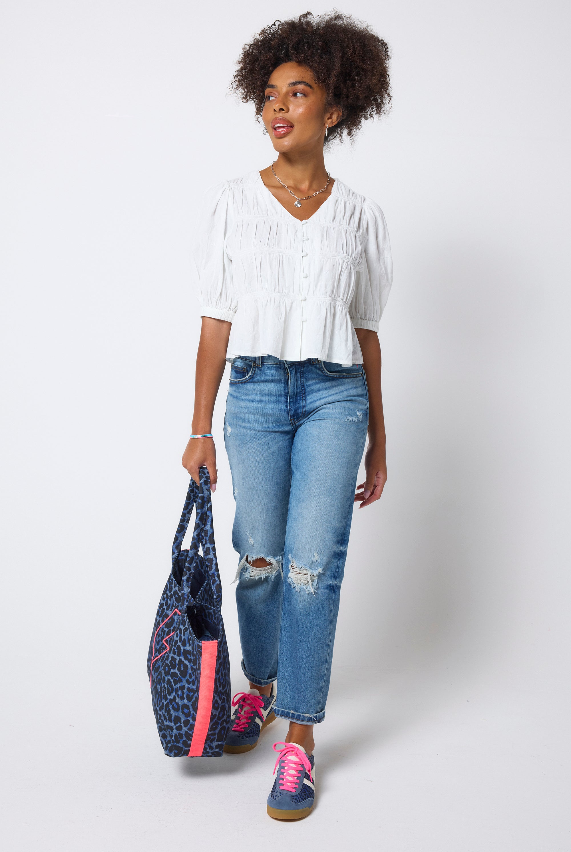 Scamp & Dude White Puff Sleeve Smocked Blouse | Model wears a short sleeve smocked blouse with distressed blue jeans and trainers.