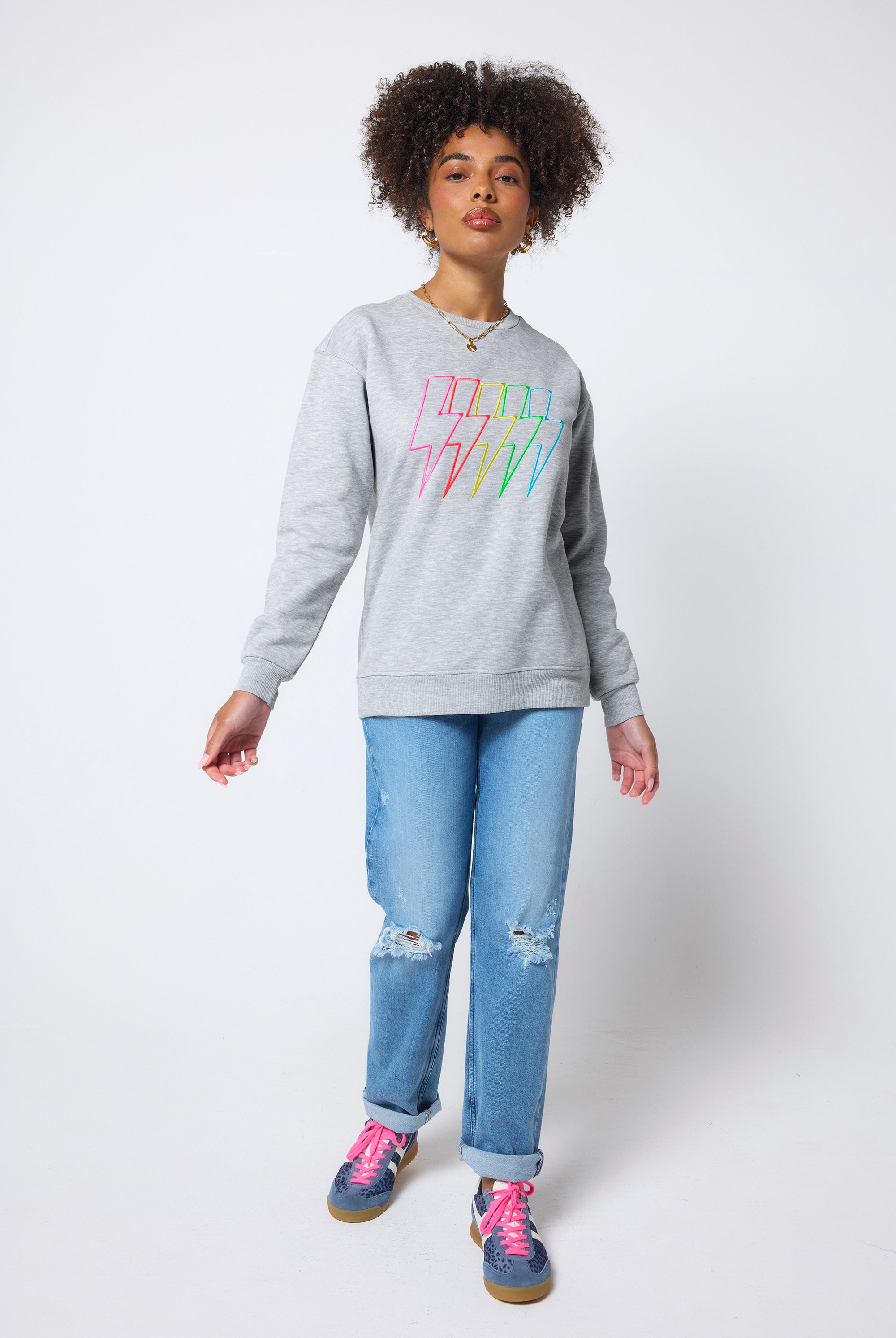 Scamp & Dude Grey Marl Multi Neon Bolt Longline Sweatshirt | Model wearing a grey longline sweatshirt with neon bolt detail. Worn with distressed blue jeans and blue trainers.