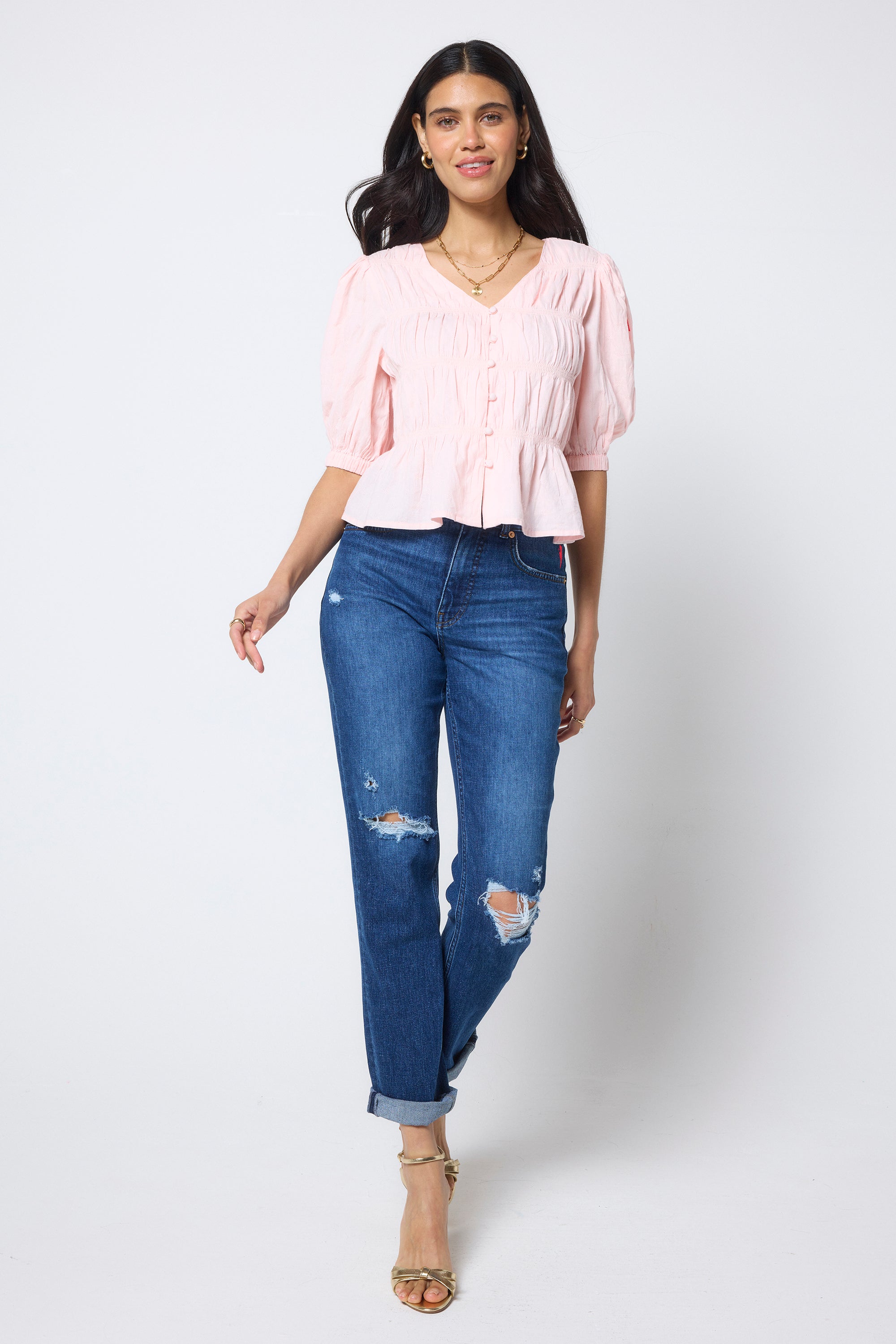 Scamp & Dude Pink Puff Sleeve Smocked Blouse | Model wears a smocked short sleeve blouse with a pair of distressed boyfriend jeans and heels.