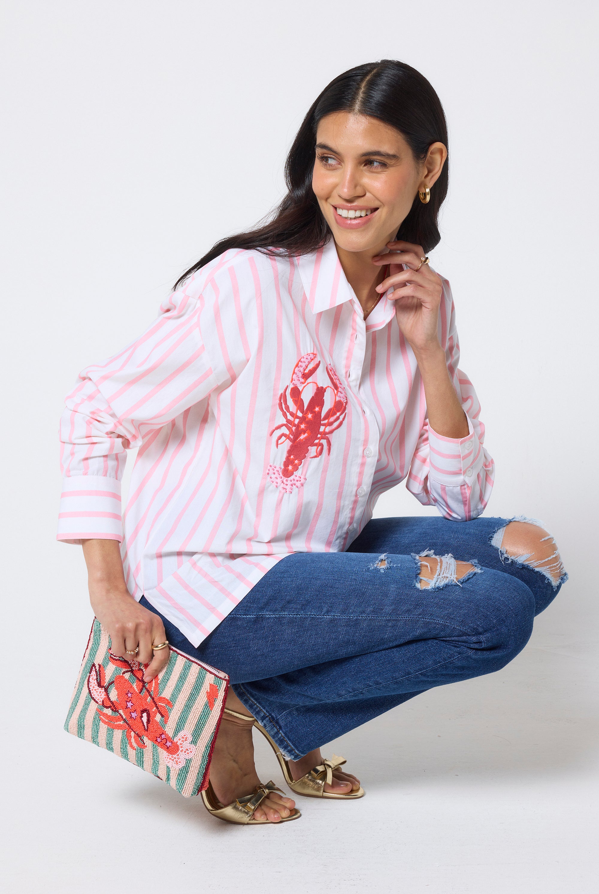 Scamp & Dude Peach & White Stripe Lobster Embellishment Shirt | Model wearing a peach striped shirt with a red lobster design and blue jeans, holding a matching clutch.