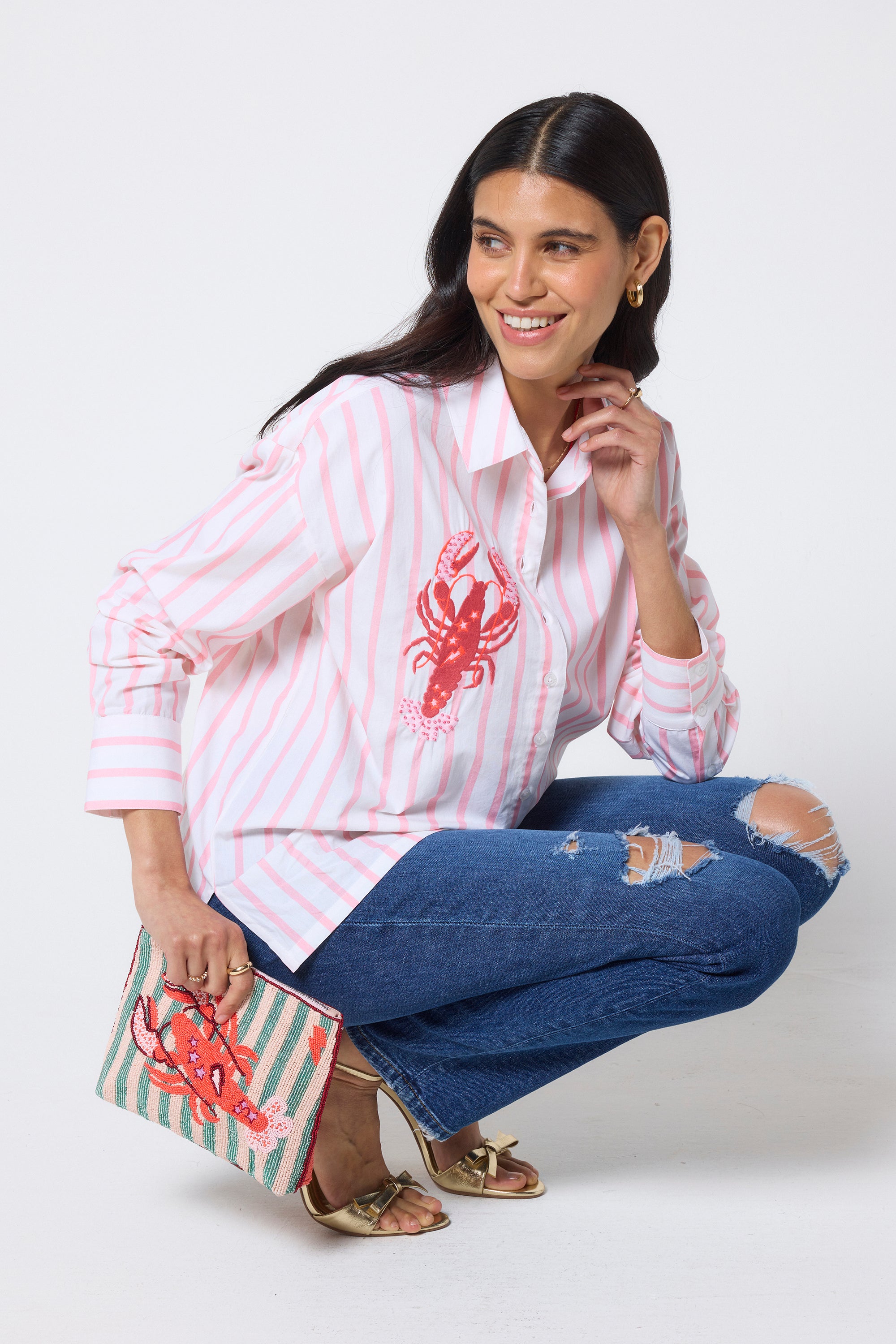 Scamp & Dude Peach & White Stripe Lobster Embellishment Shirt | Model wearing a peach striped shirt with a red lobster design and blue jeans, holding a matching clutch.
