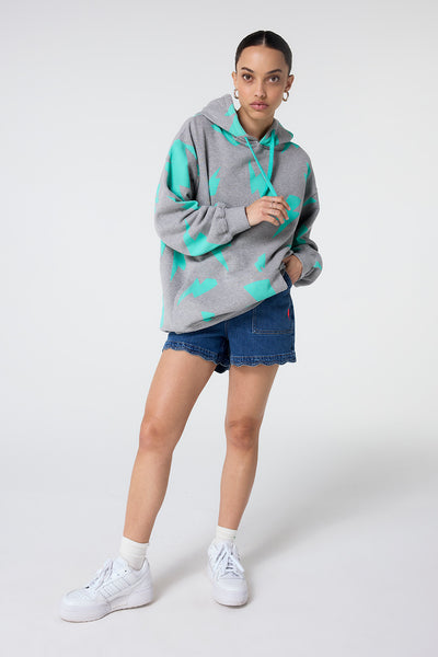 Scamp and Dude Grey Marl with Turquoise Mega Lightning Bolt Longline Hoodie | Model wearing grey marl hoodie featuring large turquoise lightning bolt repeat print with turquoise drawstrings. Paired with scallop hem denim shorts.