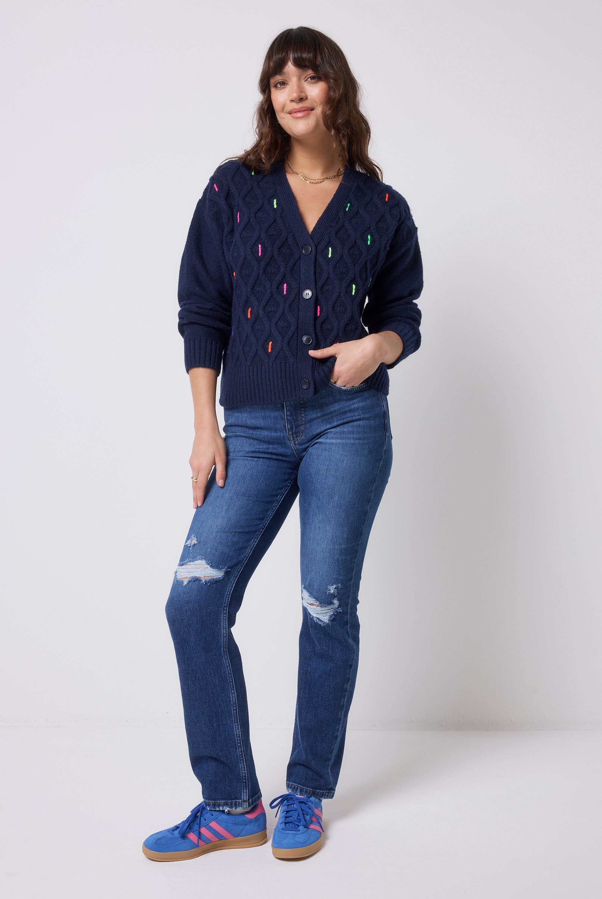 Scamp & Dude Navy with Neon Rainbow Flecks Cable Knit Cardigan | Model wearing a navy cardigan with colourful neon flecks and blue jeans.