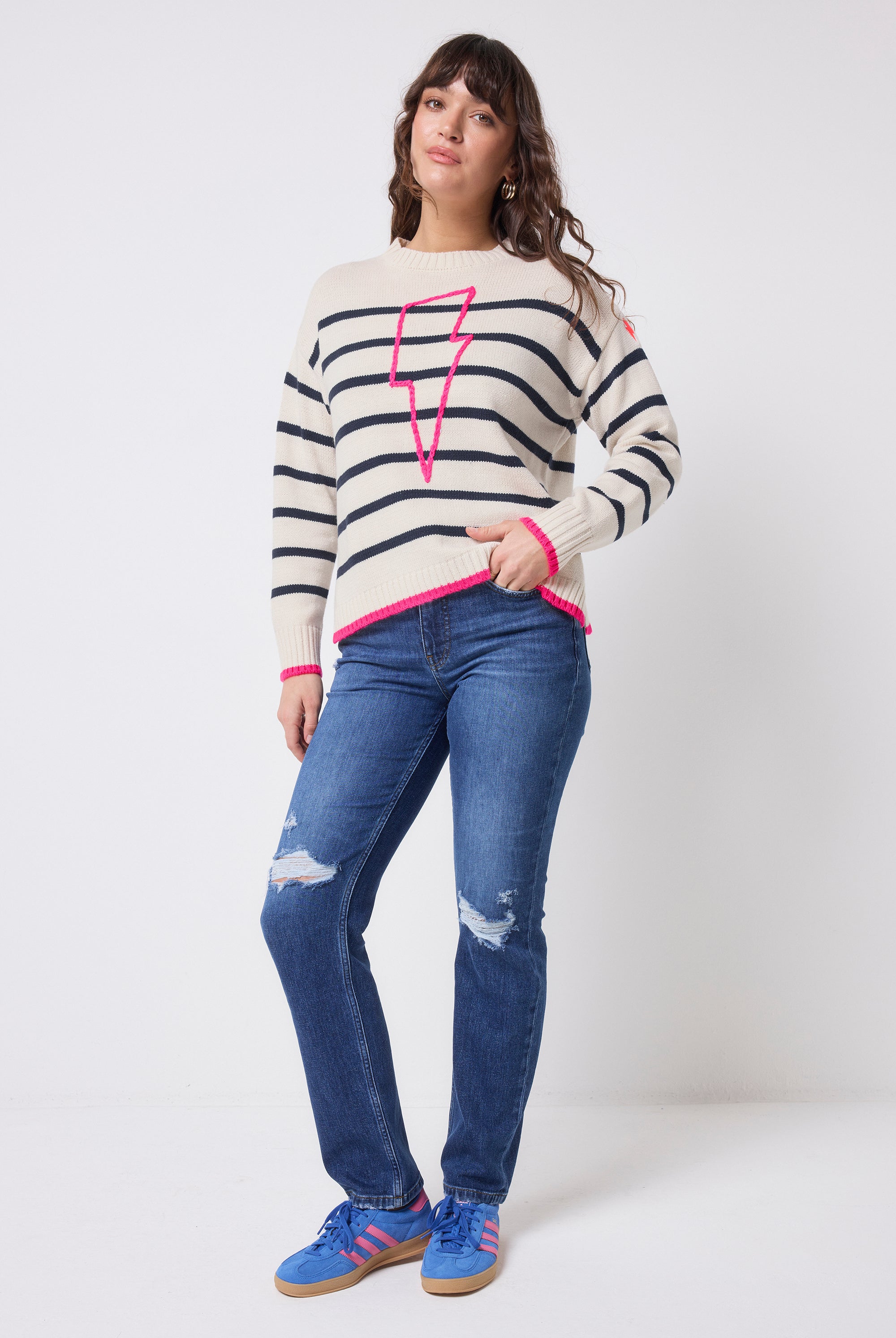 Scamp and Dude Cream with Navy Breton Stripe Knit Jumper | Model wearing distressed blue denim jeans with a stripe knit jumper that features a neon pink embroidered bolt on the front.