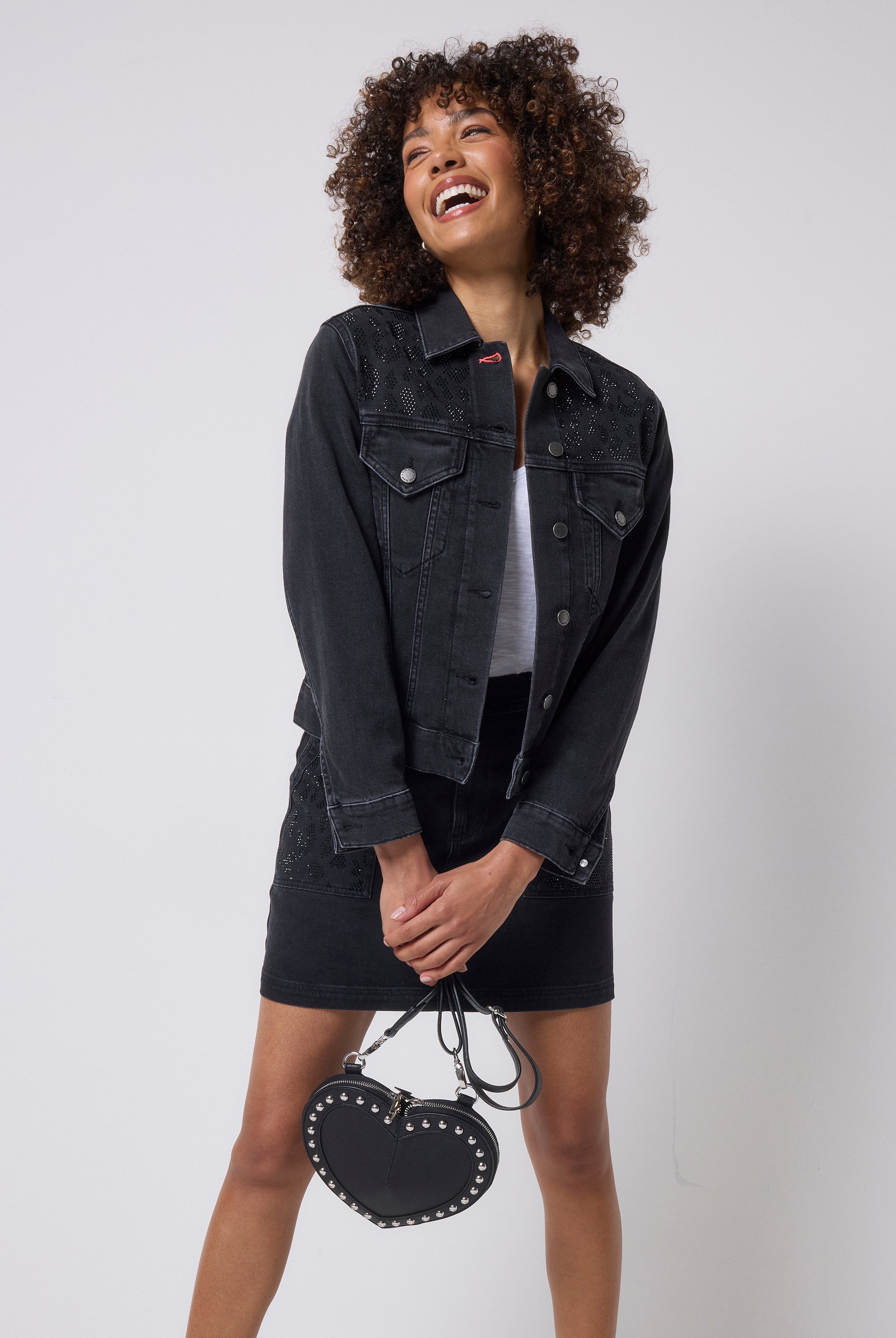 Scamp & Dude Washed Black Embellished Leopard Denim Jacket | Model wearing a black denim jacket and mini skirt with embellished detail holding a heart shaped bag.