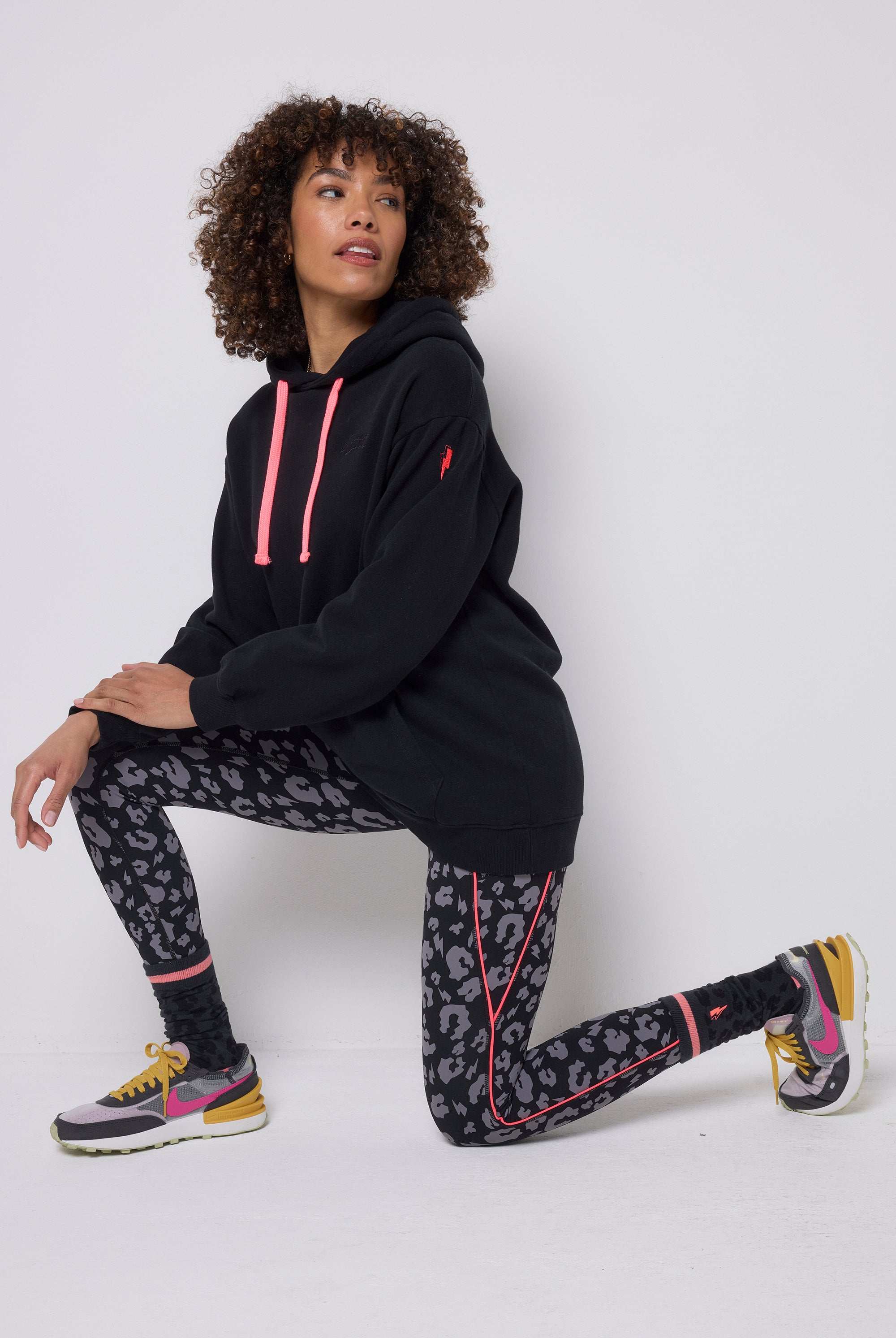Scamp & Dude Black with Grey Leopard Full Length Active Leggings | Model wearing a pair of black activewear leggings with grey leopard print on them. Paired with a black longline hoodie, black socks and trainers.