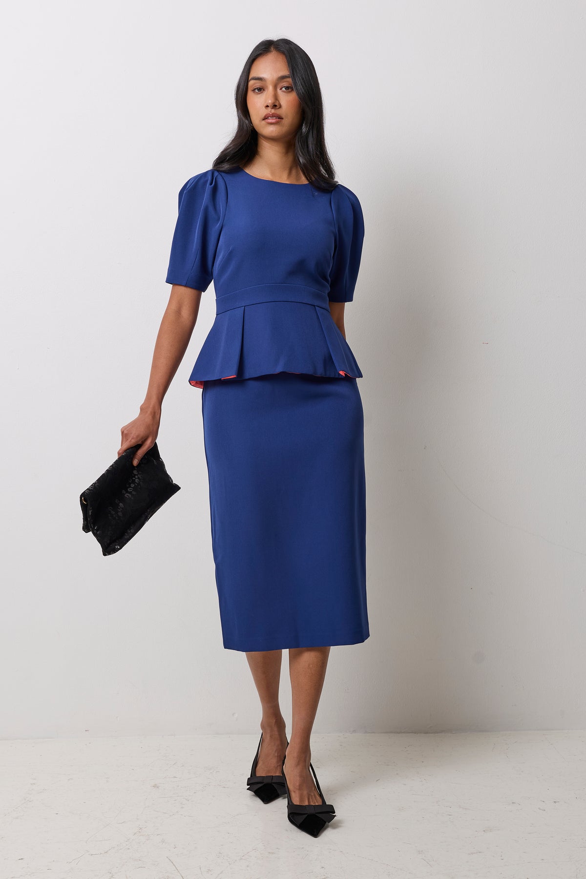 Scamp & Dude Navy Structured Peplum Midi Dress | Model wearing a blue peplum midi dress with black heels and a black bag.