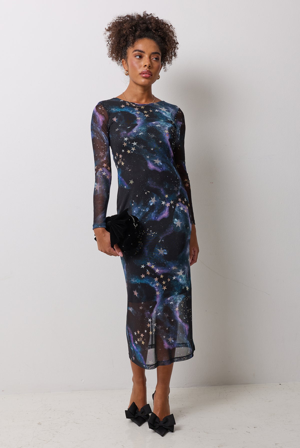 Scamp & Dude Black Galaxy Mesh Midi Dress | Model wearing a black galaxy print mesh midi dress with black bow heels and a matching bag.