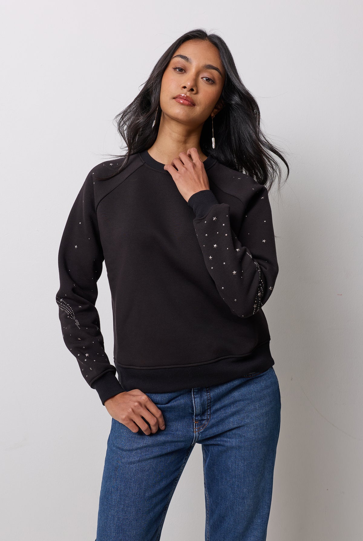Scamp & Dude Black Written In The Stars Studded Sweatshirt | Model is wearing a black sweatshirt with the star stud detail and blue jeans.