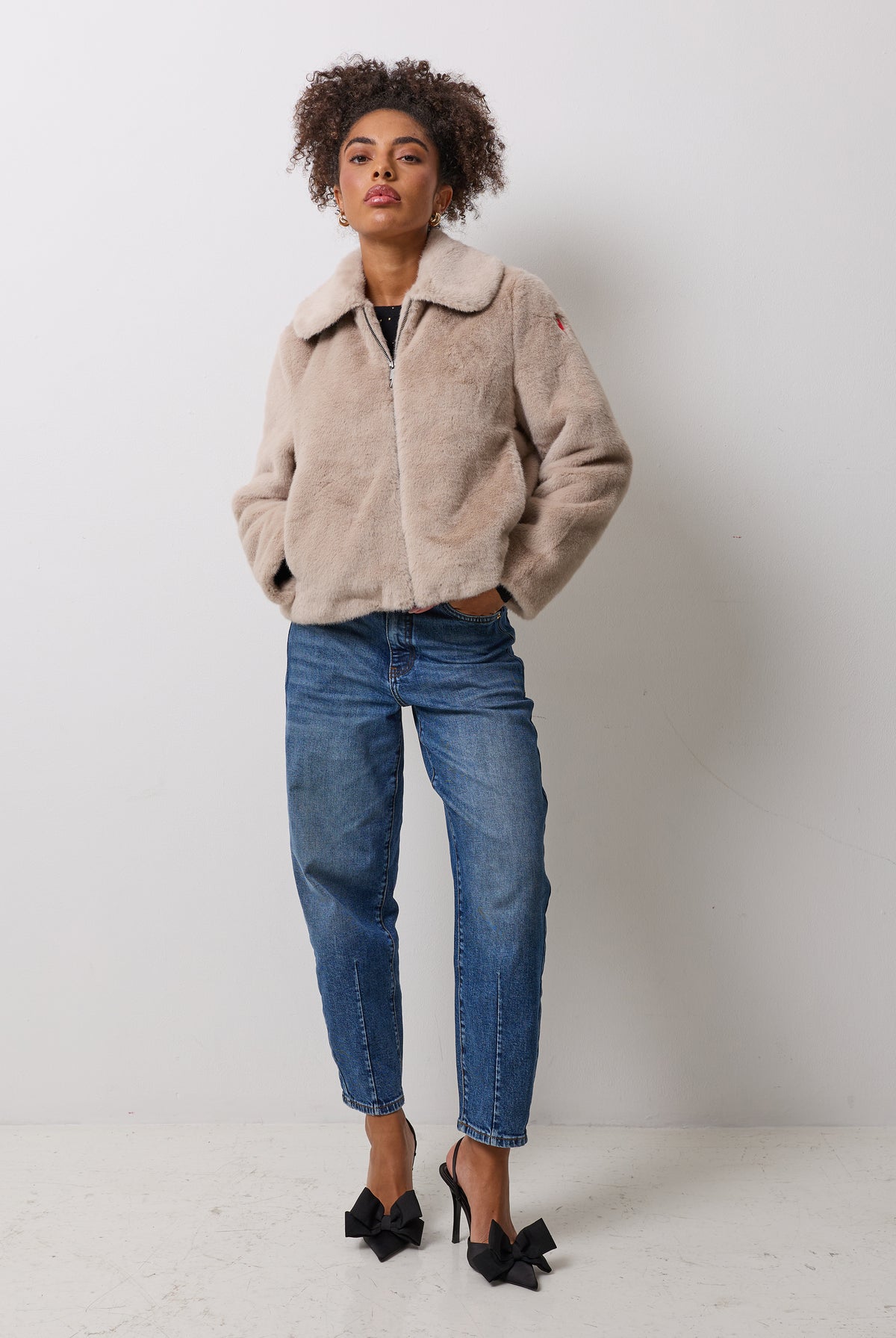 Scamp and Dude Cream Faux Fur Jacket | Model wearing blue jeans with a faux fur jacket and black bow heels.