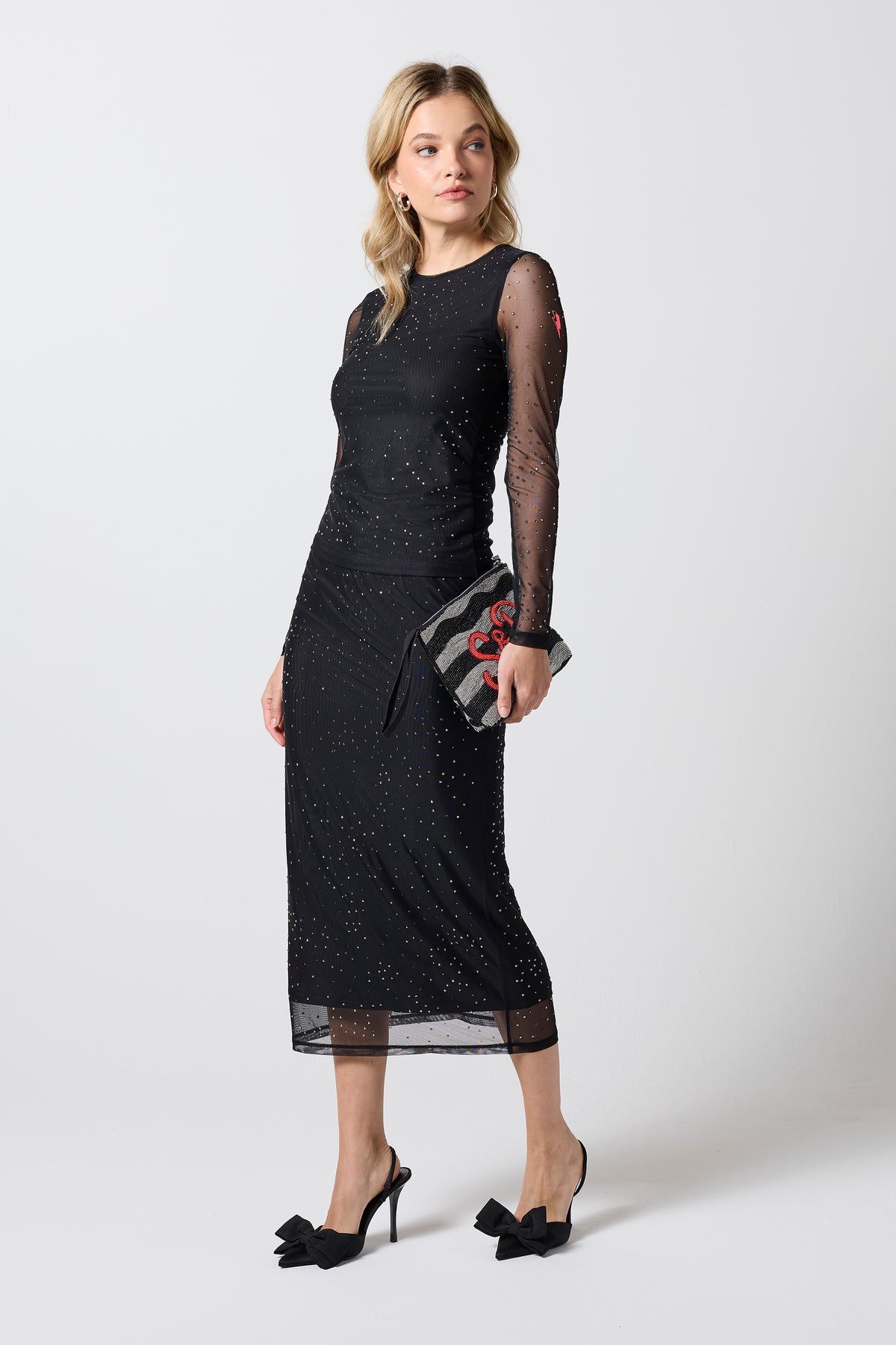 Scamp & Dude Black Embellished Mesh Midi Skirt | Model wearing a black mesh midi skirt and matching top. Worn with black bow heels and a hand beaded clutch bag.
