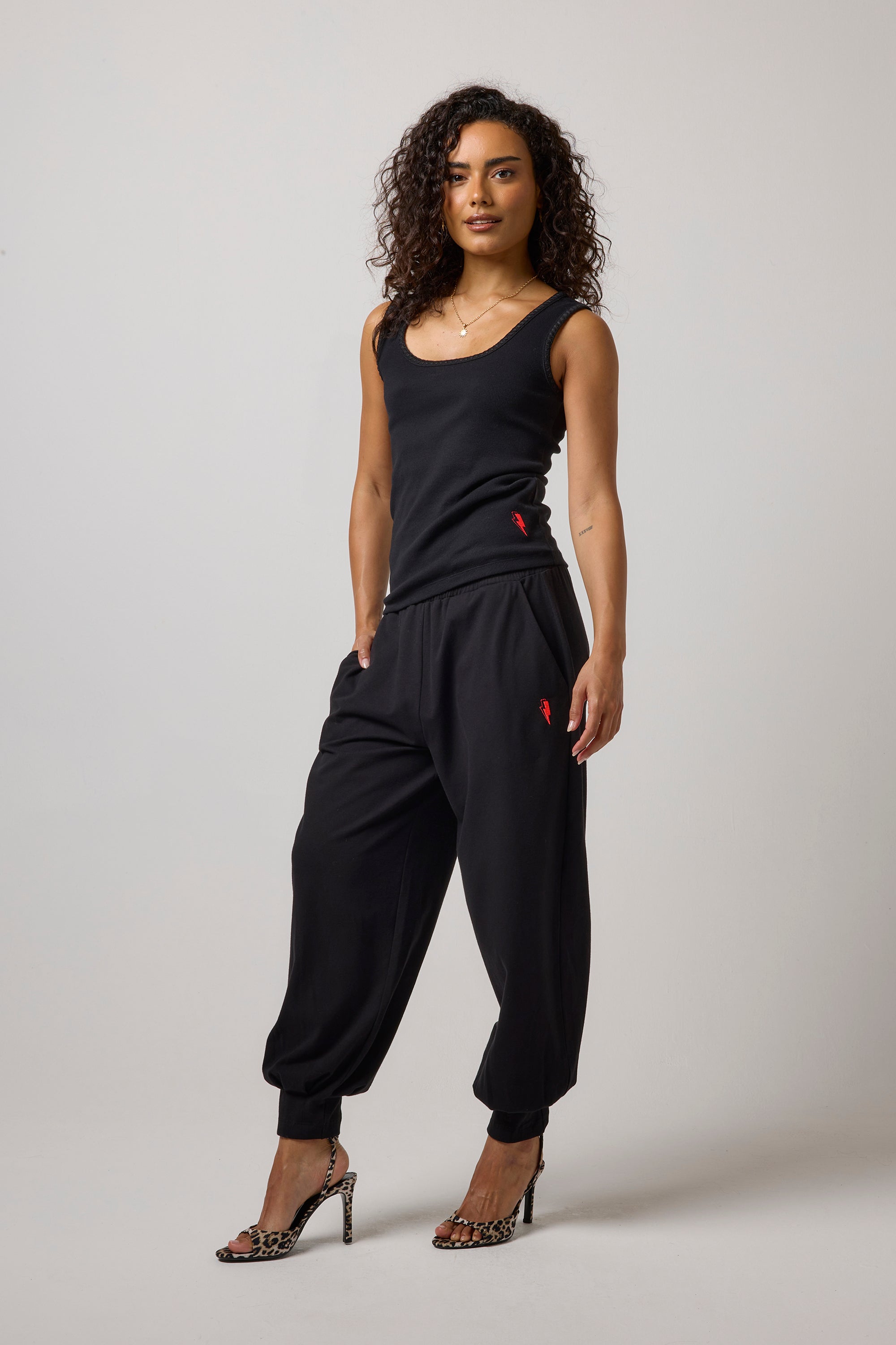 Scamp & Dude Black Barrel Joggers | Model wearing a black sleeveless vest top and matching black jogger pants and leopard heels.