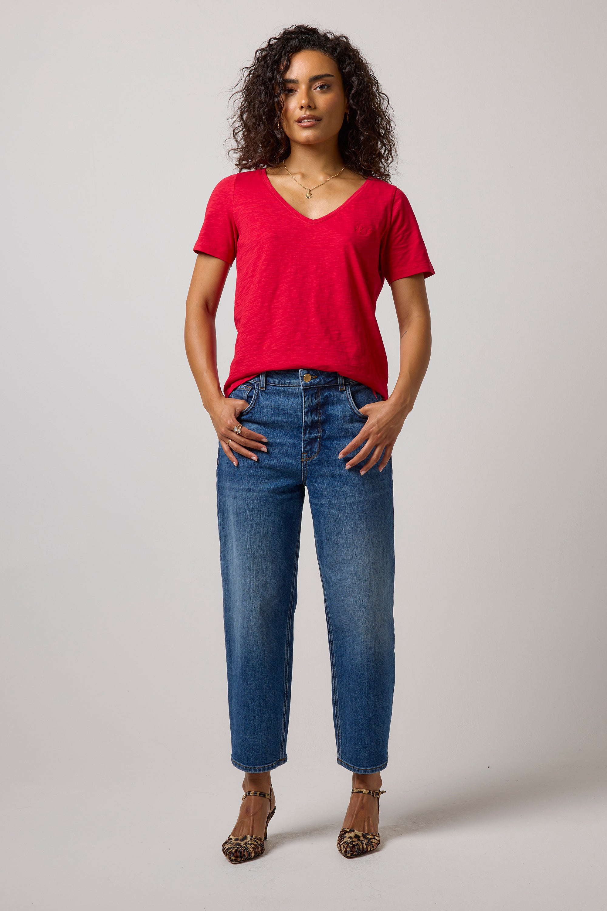 Scamp & Dude Red V-Neck T-Shirt | Model wearing a red v-neck t-shirt with a pair of barrel leg jeans and high heels.