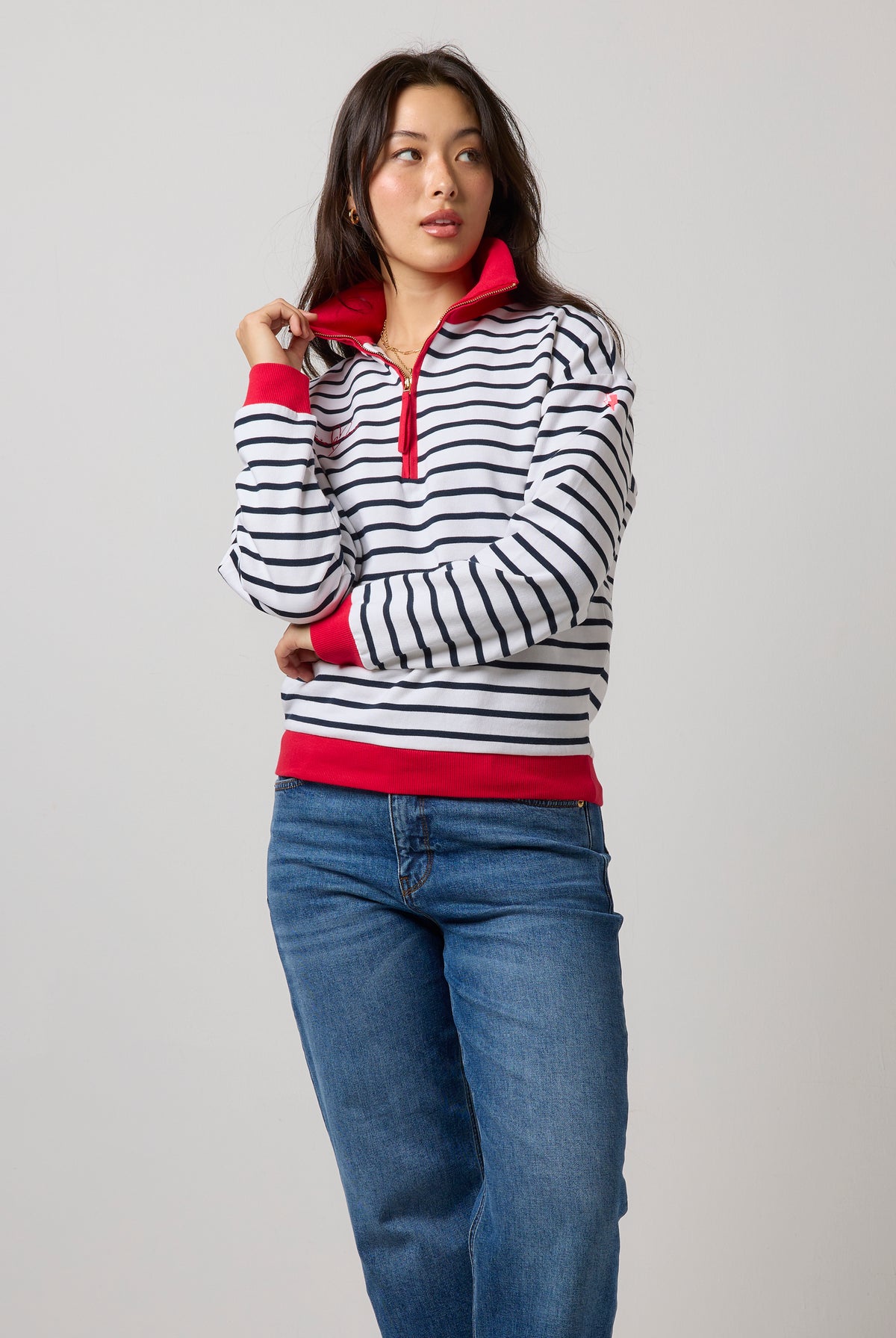 Scamp & Dude Navy Stripe Funnel Neck Sweatshirt | Model wearing a long-sleeve quarter-zip pullover with navy and white horizontal stripes, accented with bright red trim on the collar and cuffs, paired with blue jeans.