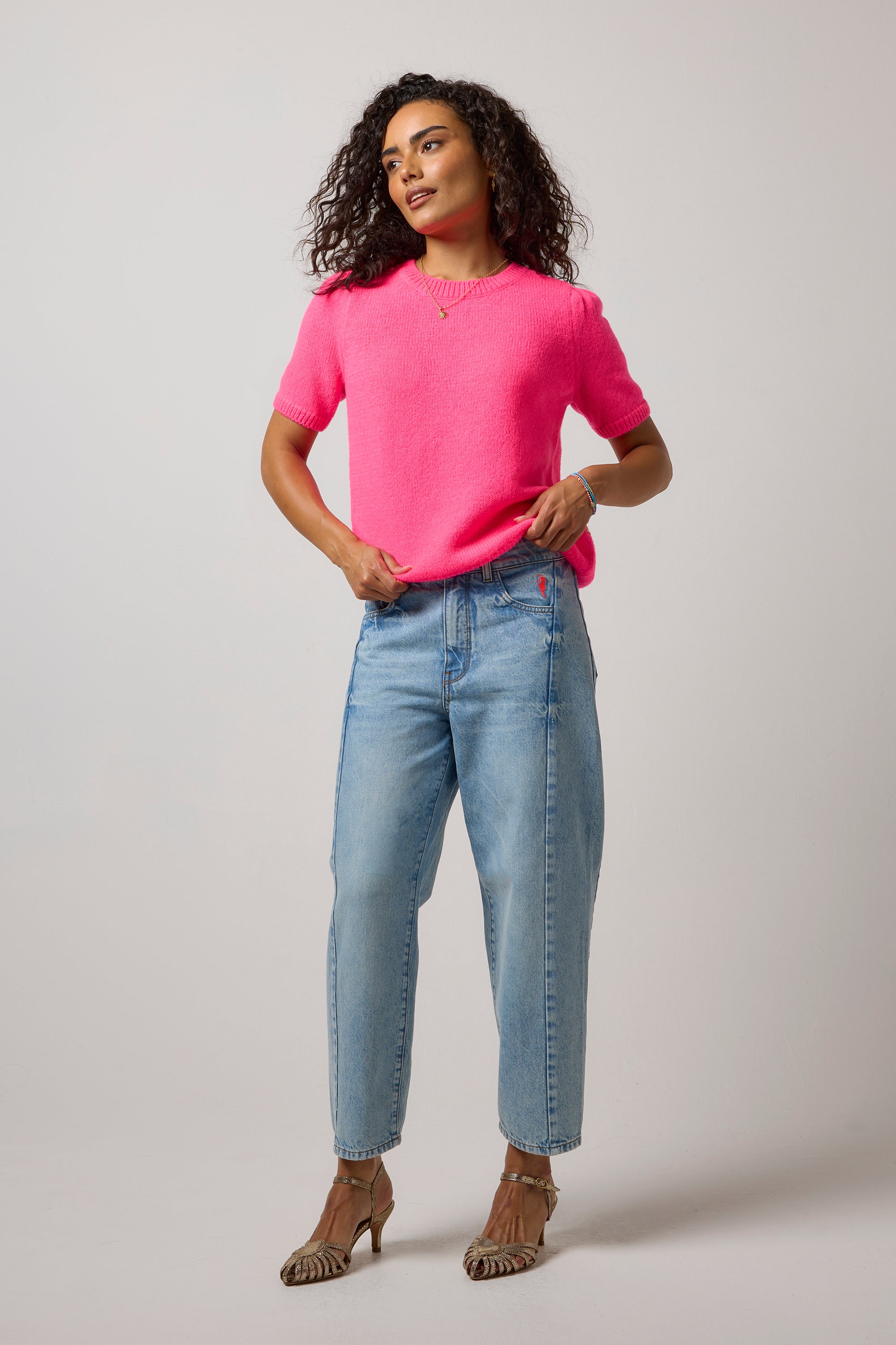 Scamp & Dude Neon Pink Short Sleeve Knit Top | Model wearing a pair of blue jeans with a pink knit top and gold heels.