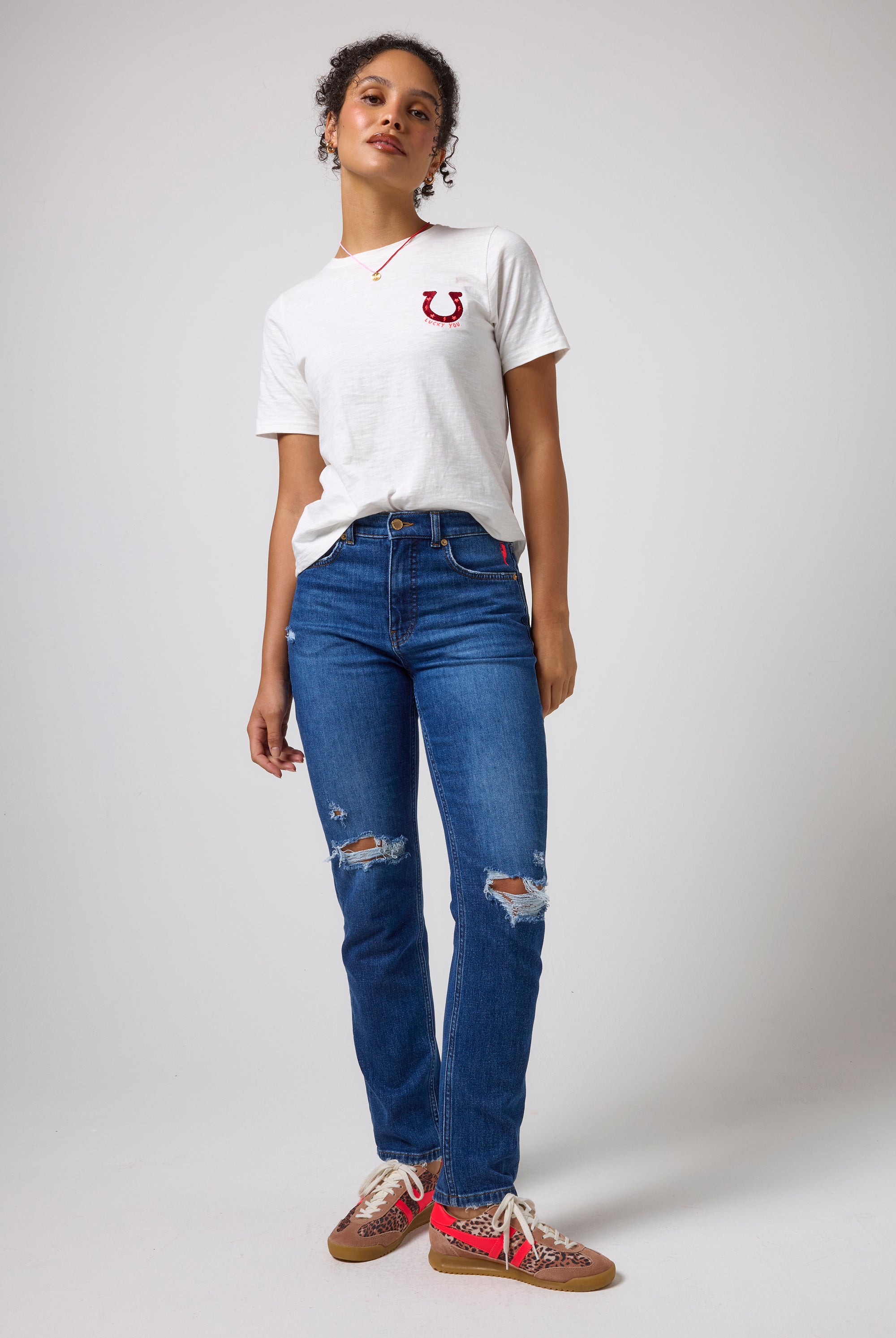 Scamp & Dude White Lucky You T-Shirt | Model wearing a white crewneck t-shirt with a red embroidered logo on the chest, paired with blue distressed jeans.