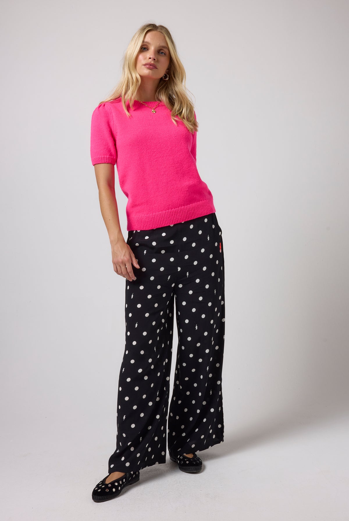 Scamp & Dude Black with White Polka Dot Bolt Wide Leg Trousers | Model wearing a pink knit top with a pair of black and white polka dot trousers.