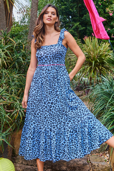 Scamp and Dude Soft Blue with Black Floral Leopard Tie Shoulder Midi Jersey Sundress | Woman wearing wearing blue leopard dress with green shrubs in the background
