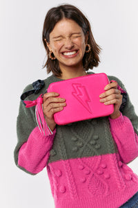Scamp and Dude Pink Leather Cross Body Bag | Model smiling wearing a knitted grey and pink jumper holding a pink leather bag with both hands 