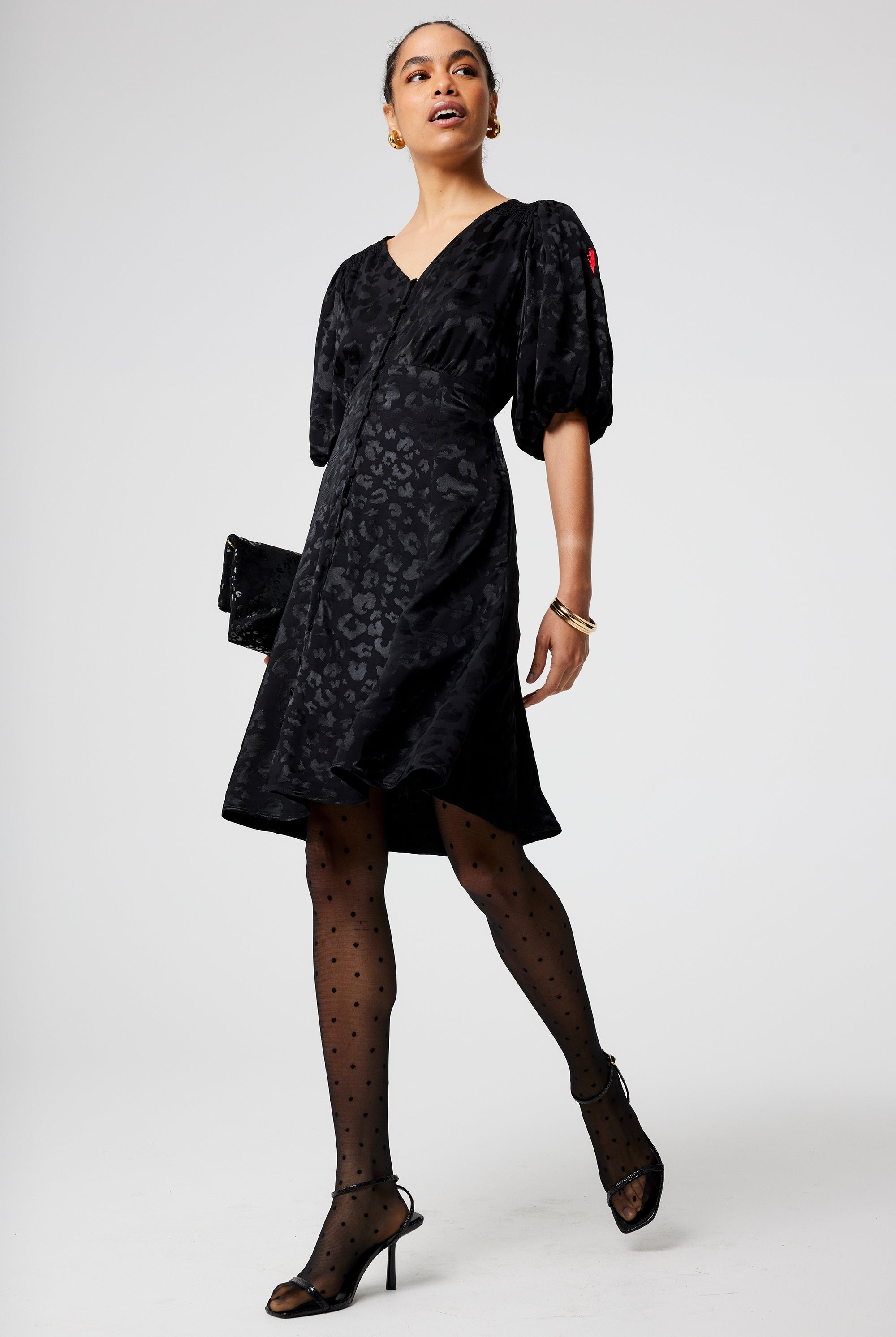 Scamp and Dude Black Jacquard Leopard Puff Sleeve Short Tea Dress | Model wearing a short v neck black tea dress in a leopard jacquard finish paired with black tights and heels.