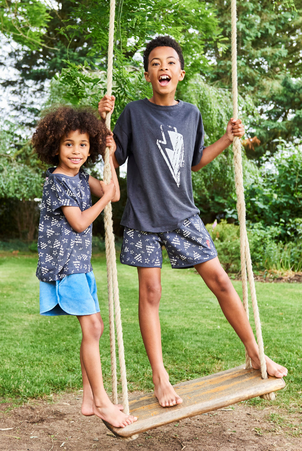 Two boys standing up on a swing wearing Scamp & Dude T-shirts and shorts