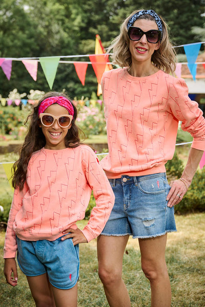Scamp and Dude Peach Lightning Bolt Long Sleeve Top | Two models, one child and one adult, wearing matching peach long sleeve tops with lightning bolt patterns in a garden 