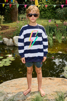 A boy wearing a navy with white stripe oversized sweatshirt with a multi-coloured neon lightning bolt on the front