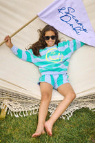 Scamp and Dude Purple and Green Striped Long Sleeve Top with Smiley Face Graphic | Child holding a flag wearing matching blue and purple striped top and shorts