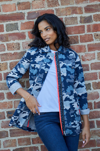 Scamp and Dude Navy Camo Utility Jacket | Model standing against a brick wall wearing a blue camo jacket with white shirt and blue jeans