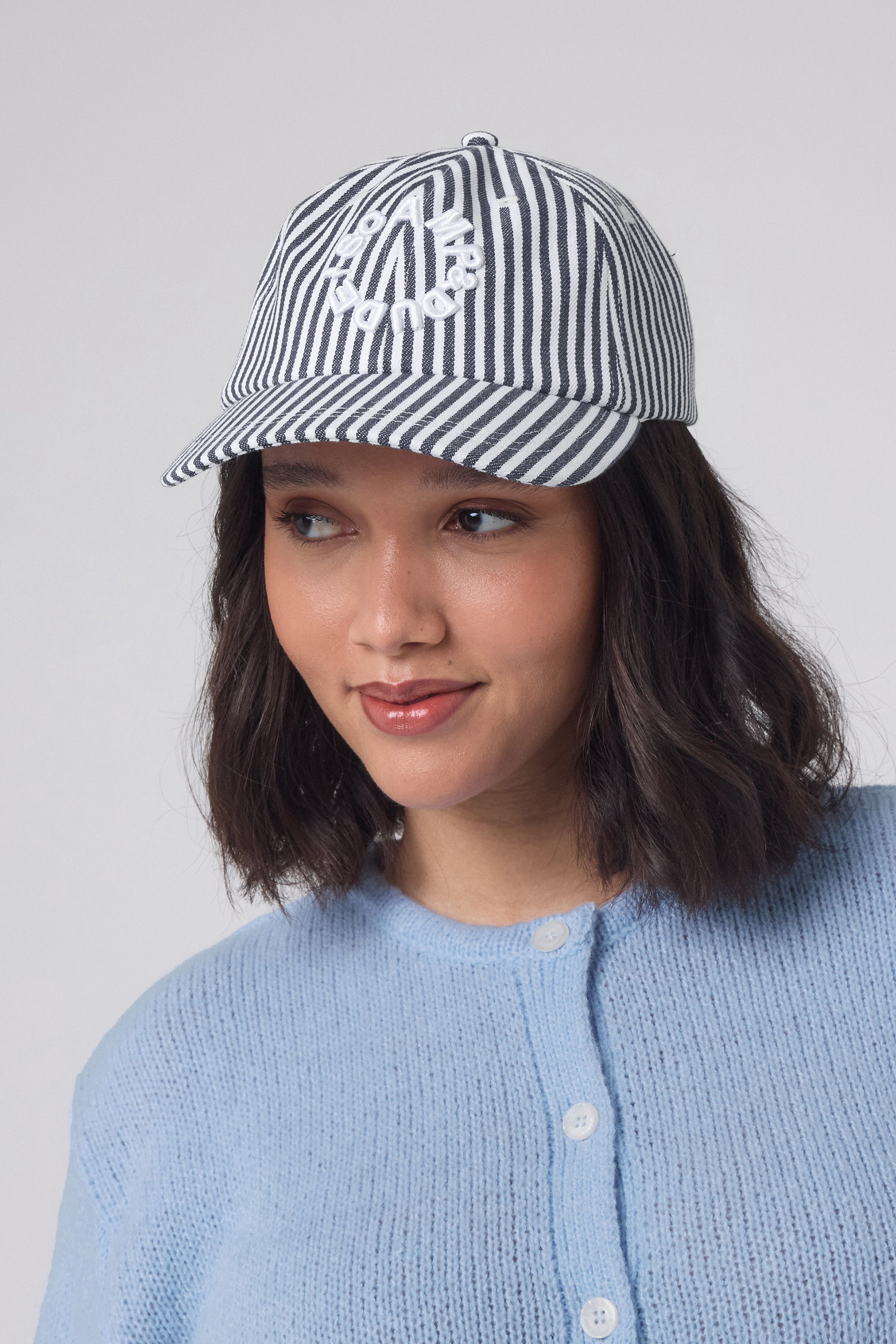 Scamp and Dude White with Navy Stripe Graphic Logo Cap | Model wearing a blue cardigan with a navy and white stripe logo cap.