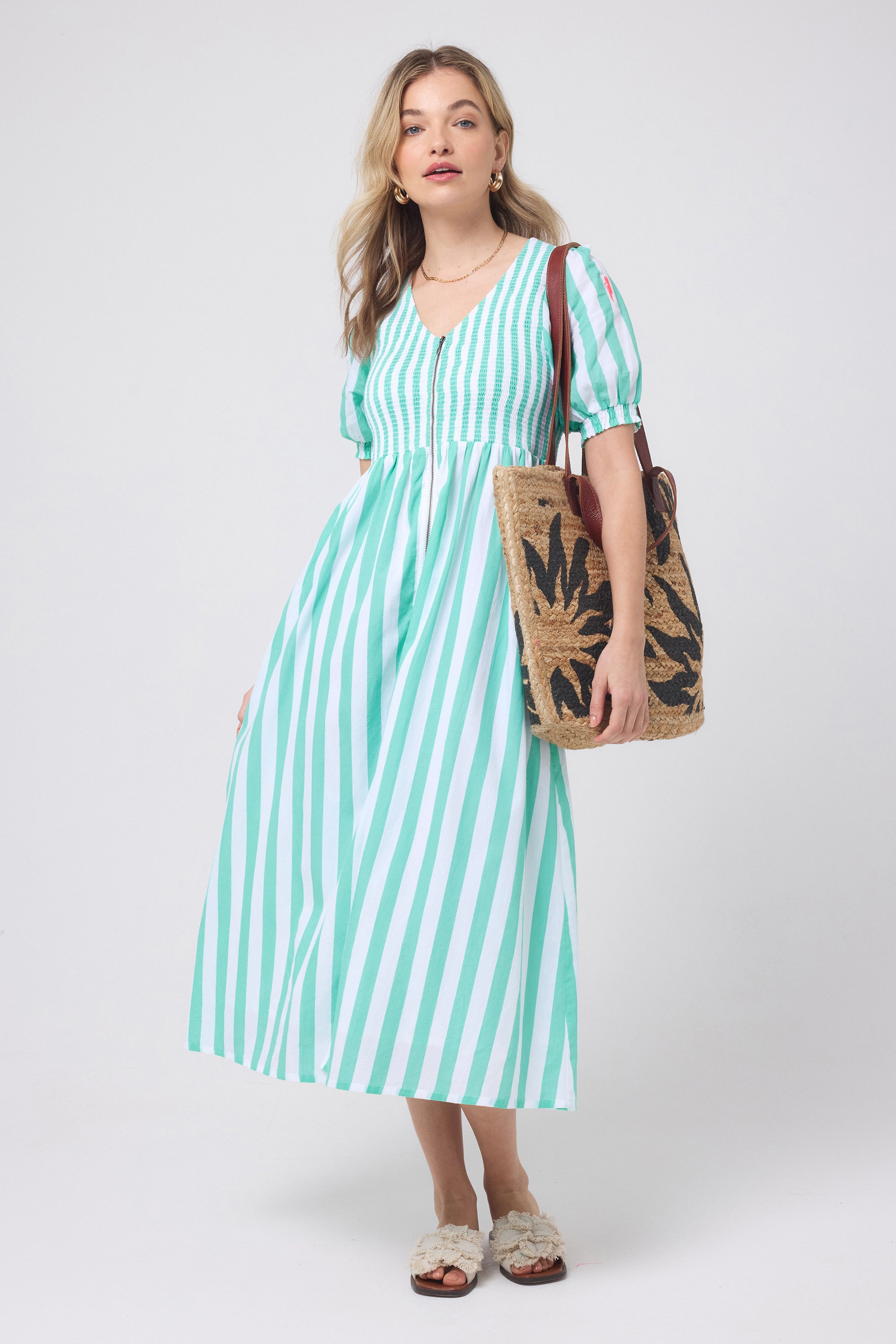 Scamp and Dude Green with White Stripe Shirred Zip Detail Midi Dress | Model wearing a green and white stripe zip front dress with neutral sandals and gold jewellery.