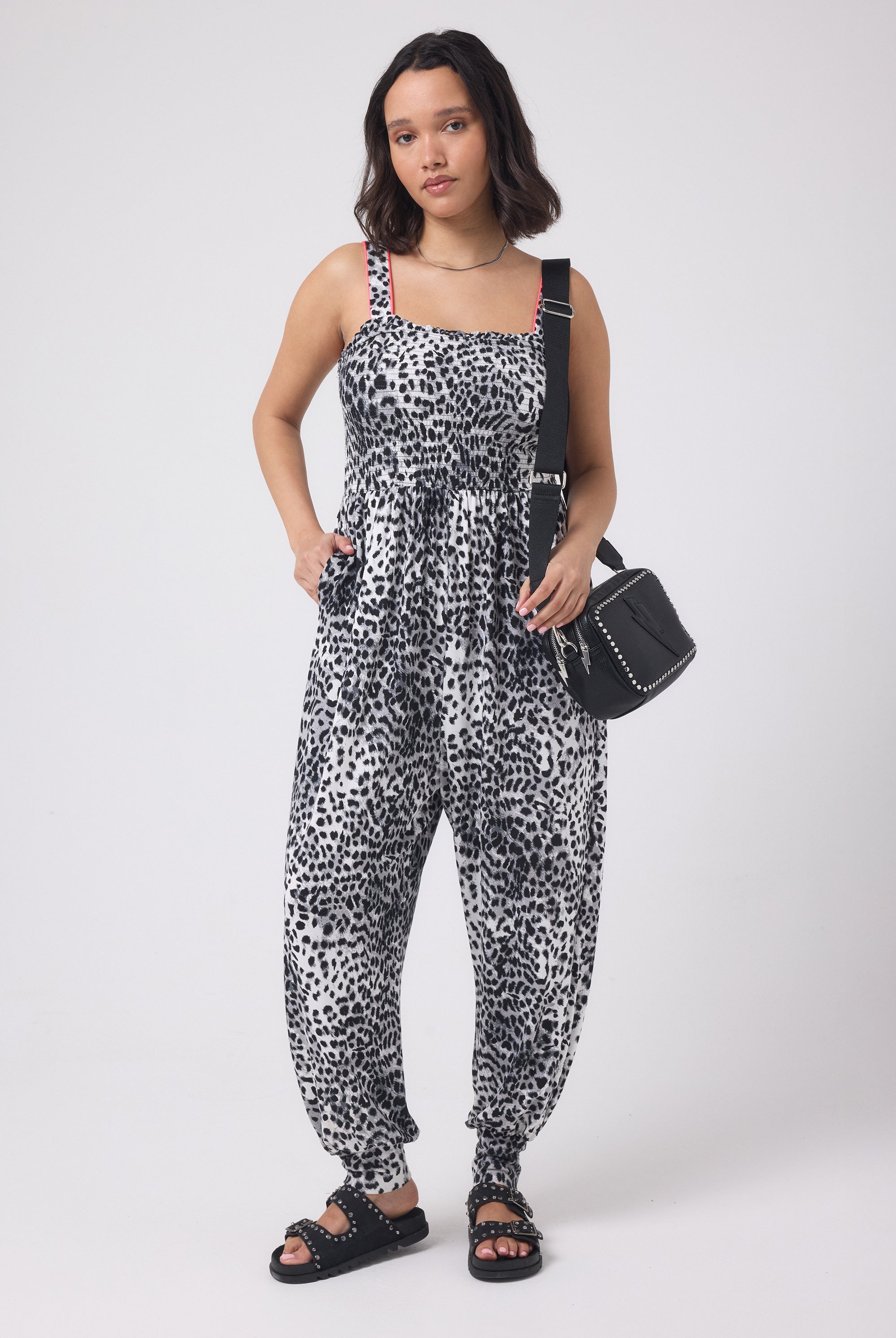 Scamp and Dude Grey with Black Cheetah Jersey Jumpsuit | Model wearing a grey and white cheetah print jumpsuit with a black cross body bag. Worn with black studded sandals.