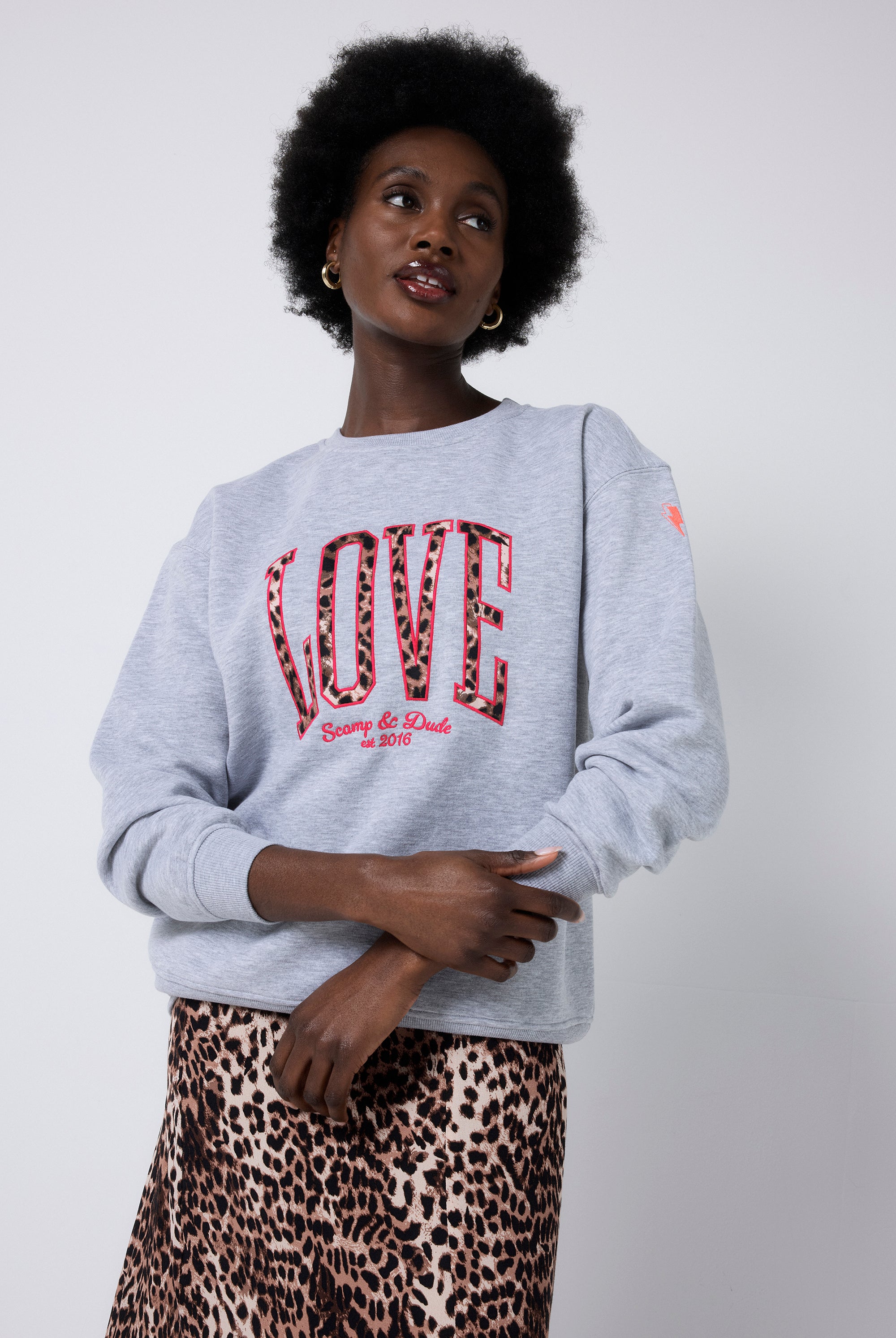 Scamp and Dude Grey Love Leopard Oversized Sweatshirt | Model wearing a grey oversized sweatshirt that features 'LOVE' Scamp & Dude logo. Paired with a cheetah print skirt.