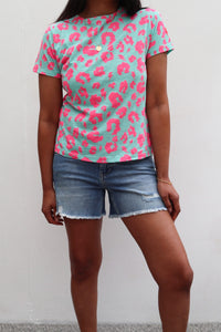 A lady wearing a green with neon pink leopard and lightning bolt print T-shirt with denim shorts