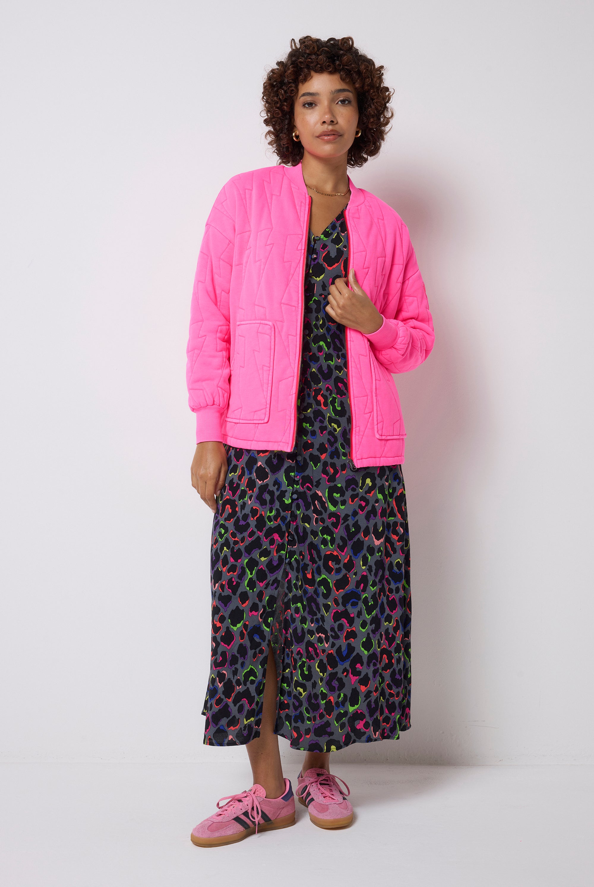 Scamp and Dude Neon Pink Lightning Bolt Regular Fit Quilted Bomber Jacket | Model wearing a pink jacket, grey dress with rainbow leopard print and pink shoes on a white background.