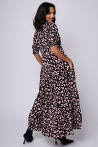 A lady with her hands in her pockets wearing a black v-neck maxi dress with pale peach leopard and lightning bolt print
