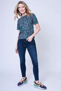 A lady wearing a pleated puff sleeve grey t-shirt with black & green leopard & lightning print with dark indigo jeans